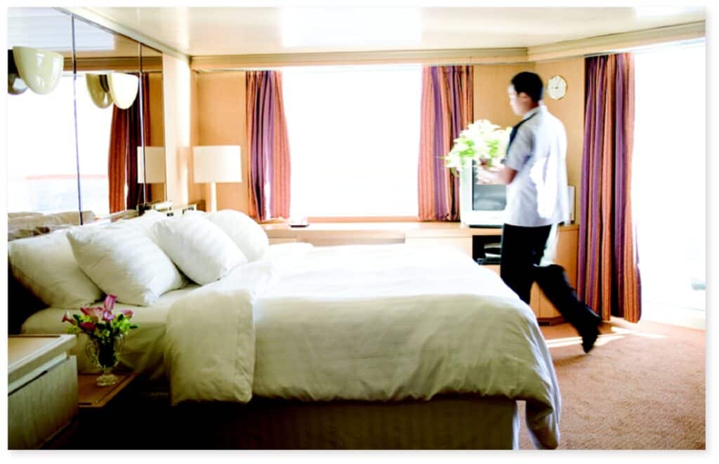 Holland America Line ship stateroom for Signature of Excellence initiative. A crewmember is placing fresh flowers next to the bed