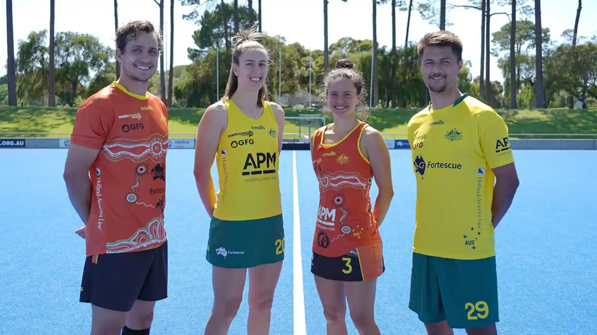 Four national field hockey players wearing yellow and orange jerseys on court.