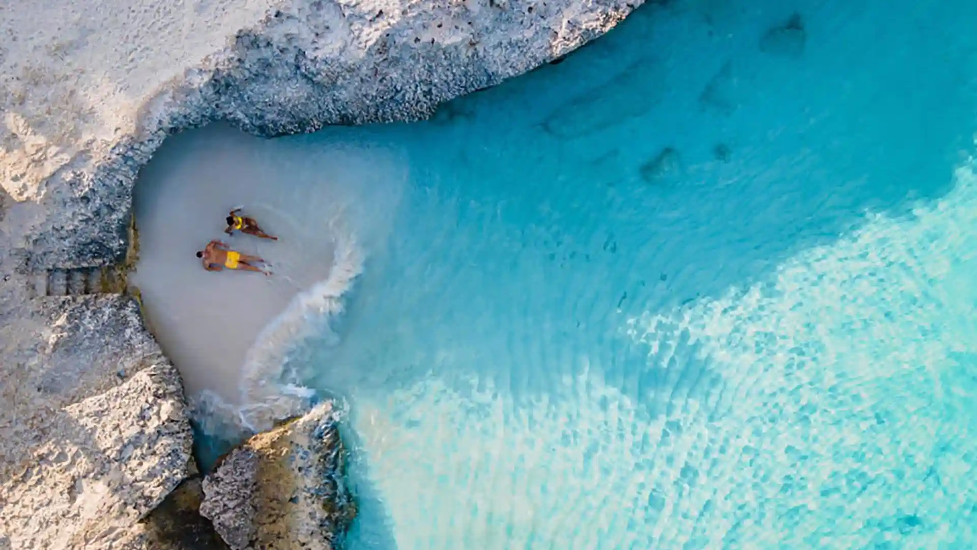 Two people relax on sand close to waves.