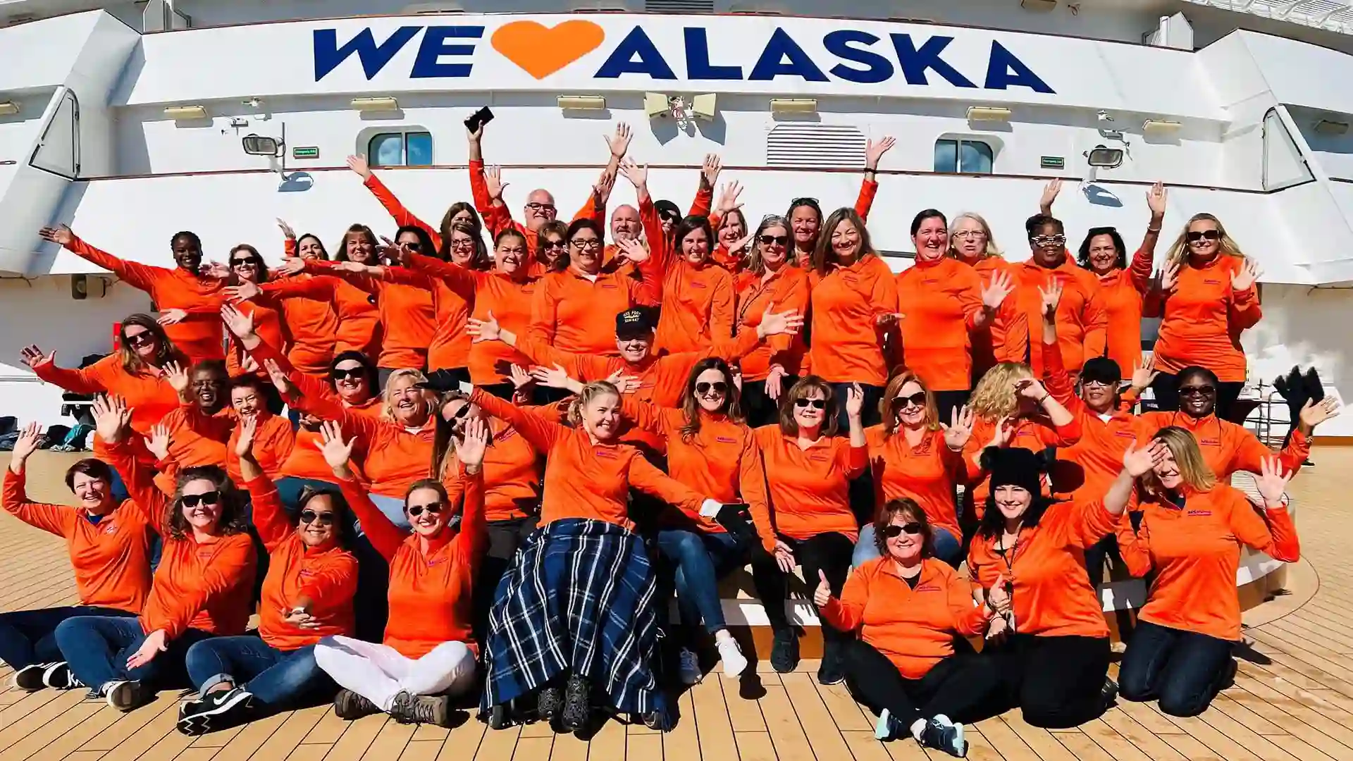 Group of Holland America Line employees wearing orange shirts gather on deck of cruise ship.