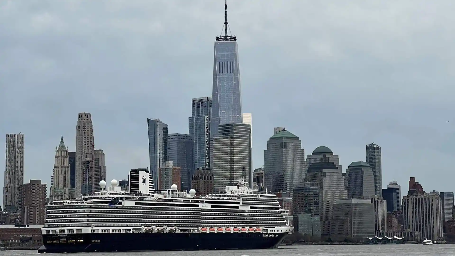 Holland America Line cruise ship sailing in front of New York City landscape.