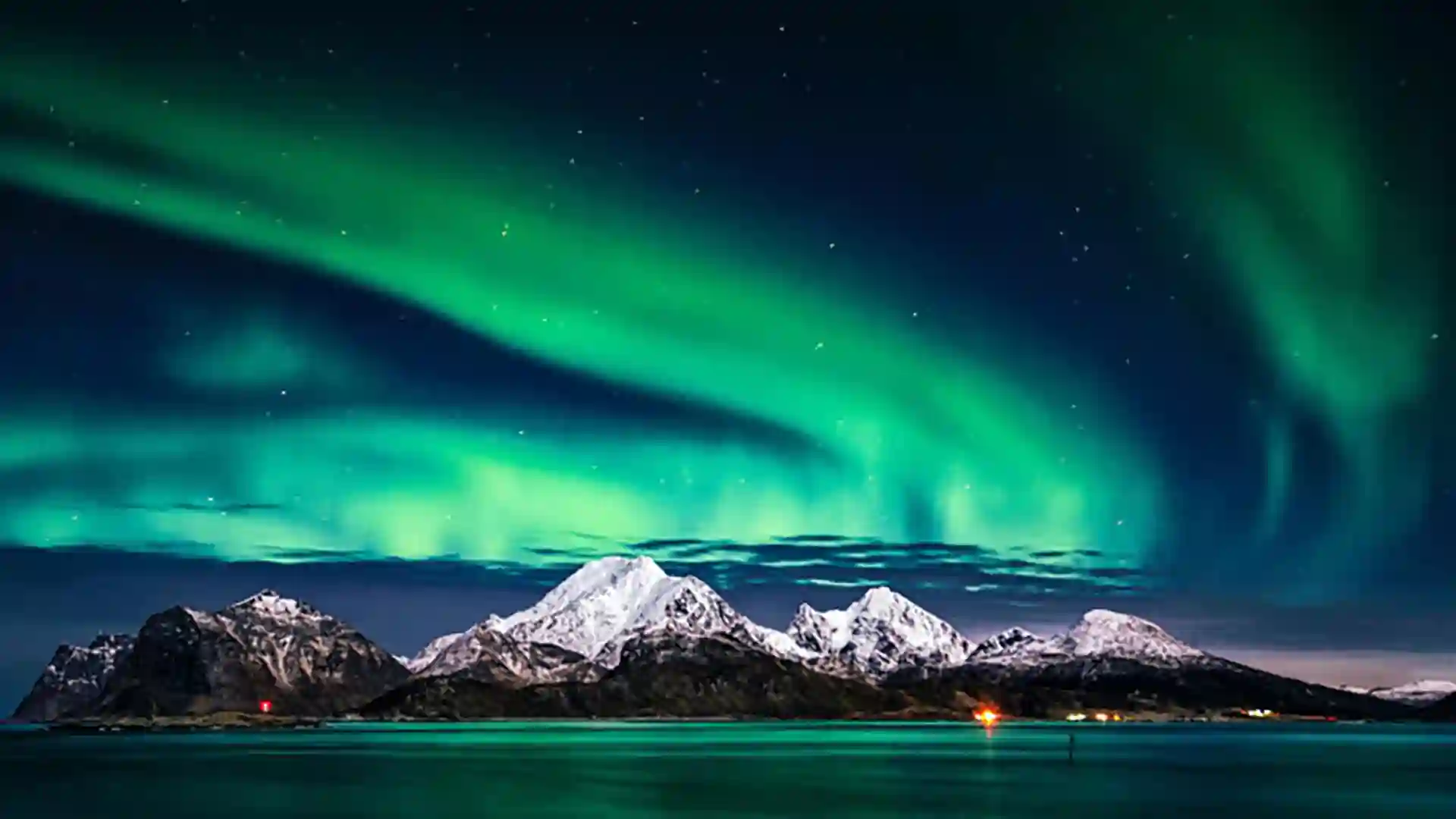 Northern_Lights_Northern_Europe Green northern lights appear above snow-capped mountains under dark night sky.