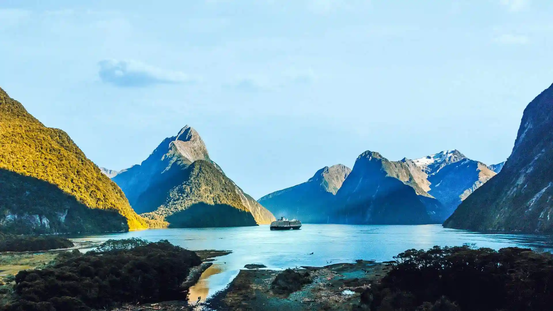View of Holland America Line cruise ship sailing around mountainous landscapes in Australia and New Zealand.
