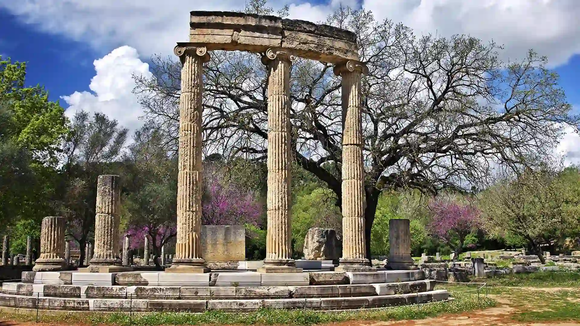Large ancient pillars frame ruins on top of steps with trees in background.