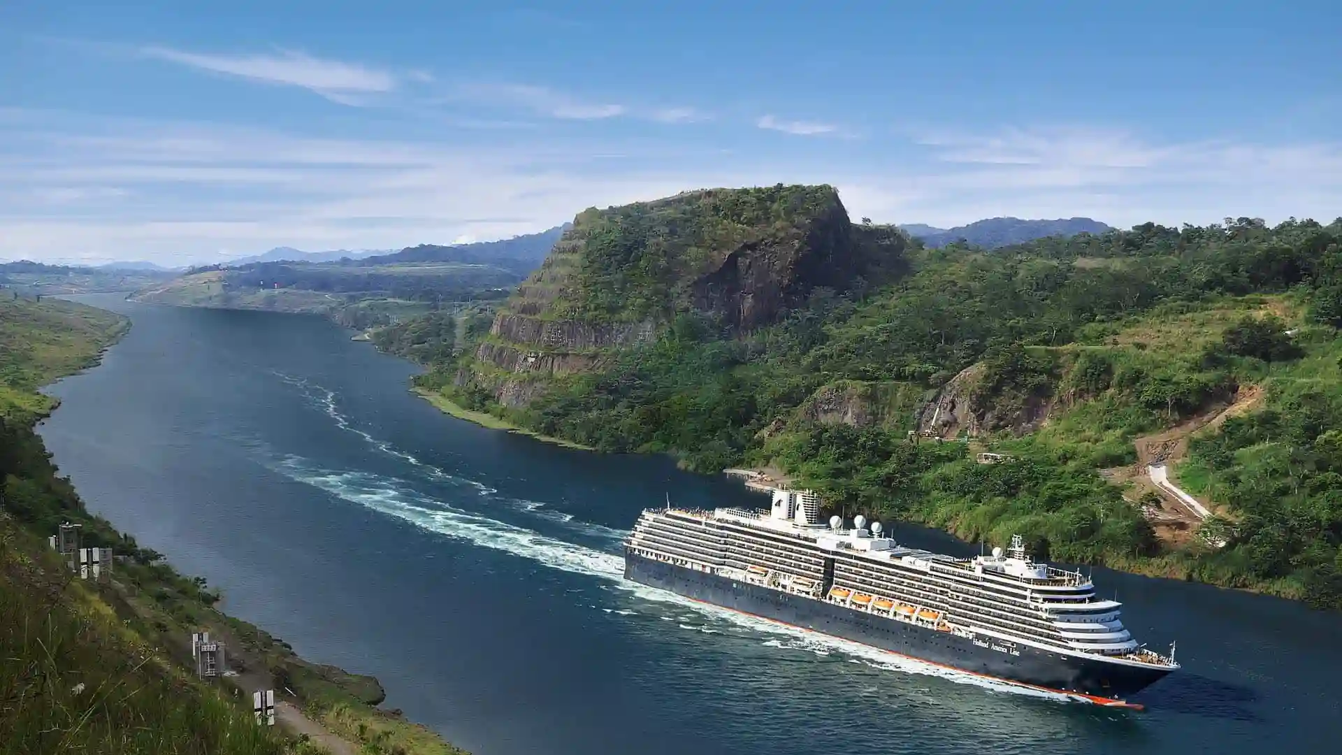 View of Holland America Line cruise ship sailing the Panama Canal between lush landscapes.