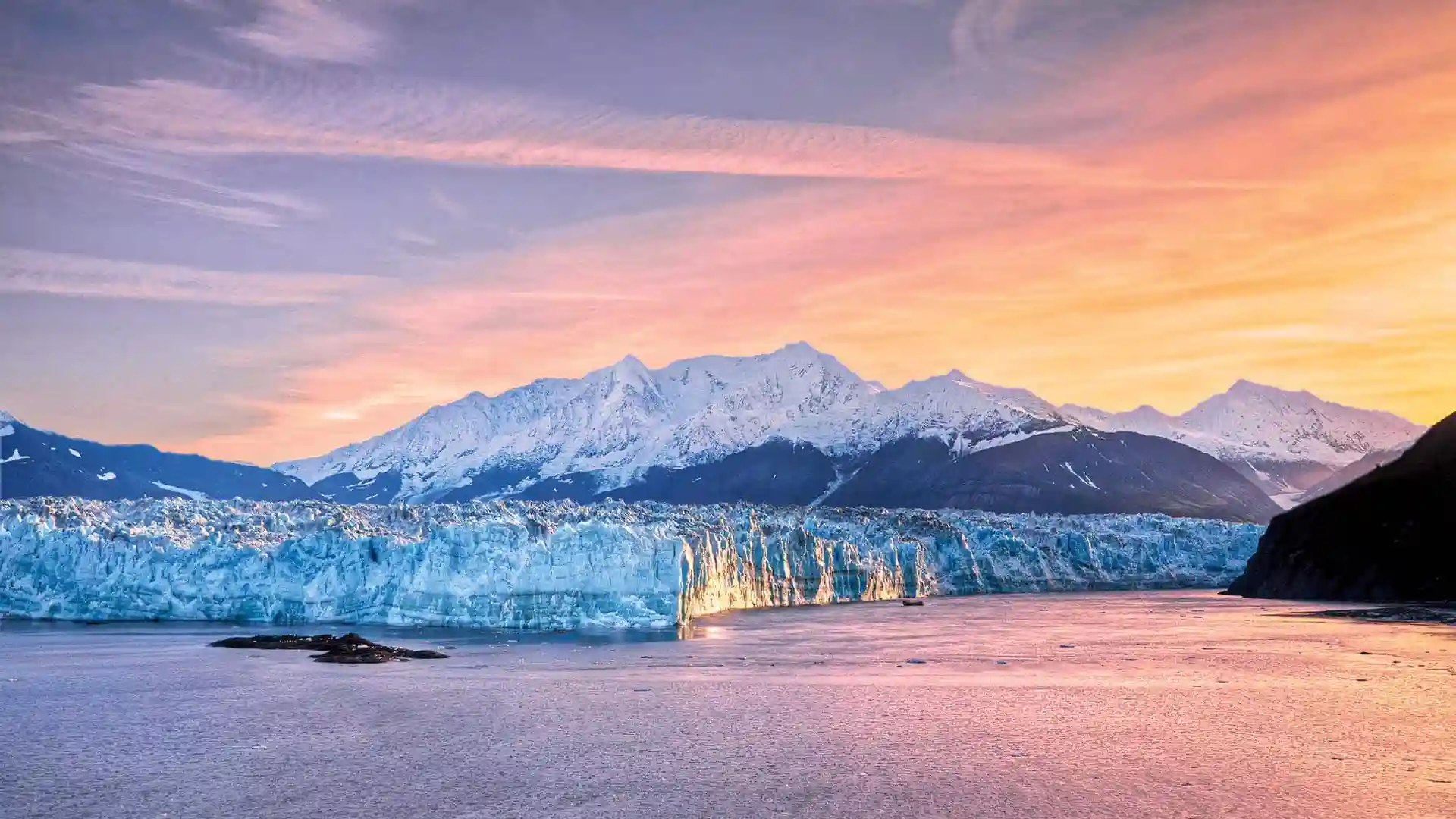 Sunlit skies over Alaska glacier and snowcapped mountains.