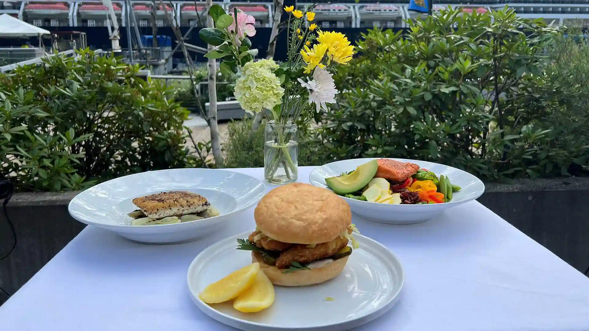 View of fresh seafood meals on table with flowers in front of Holland America Line cruise ship.