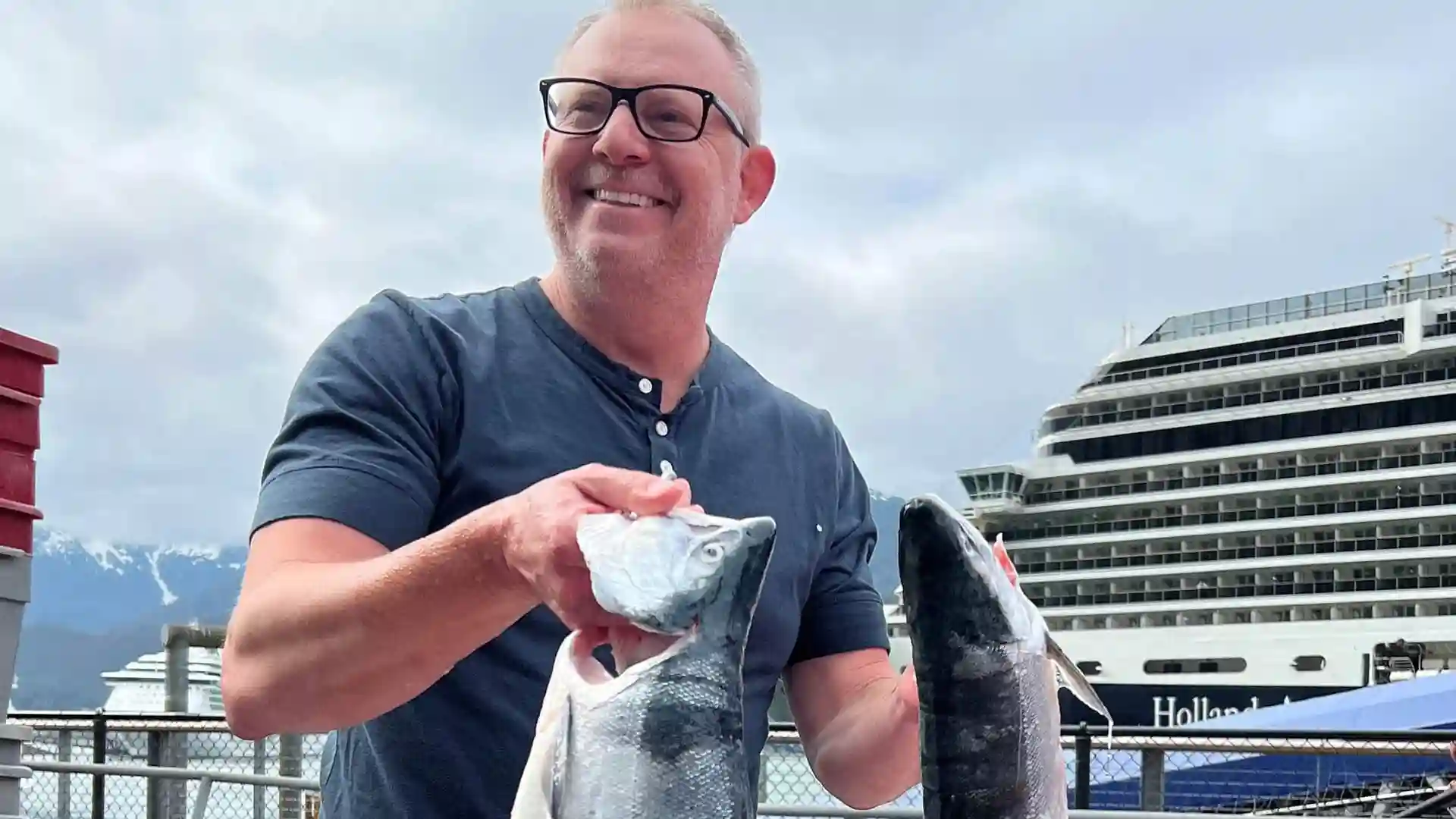 Person holding fresh caught fish in front of Holland America Line cruise ship.