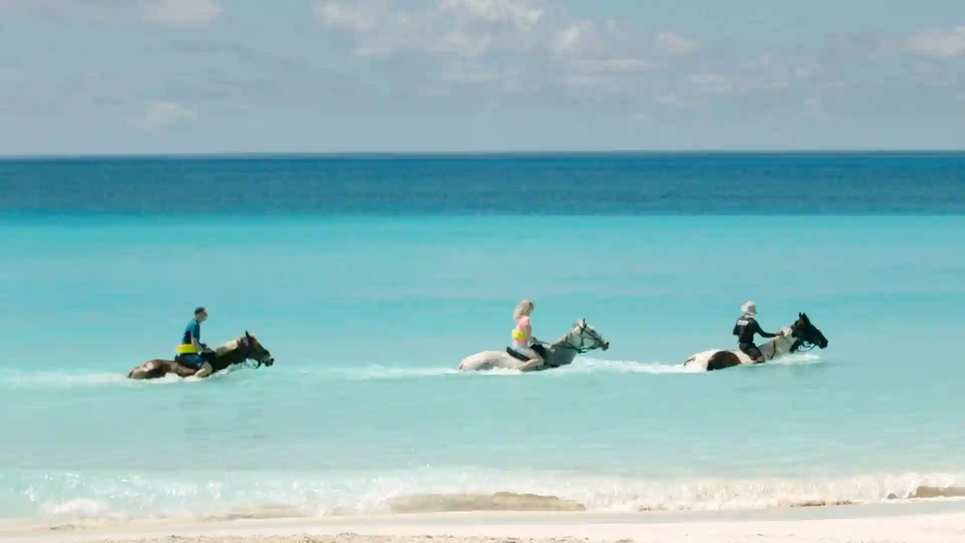 People horseback riding through shallow waters in Half Moon Cay, Bahamas.