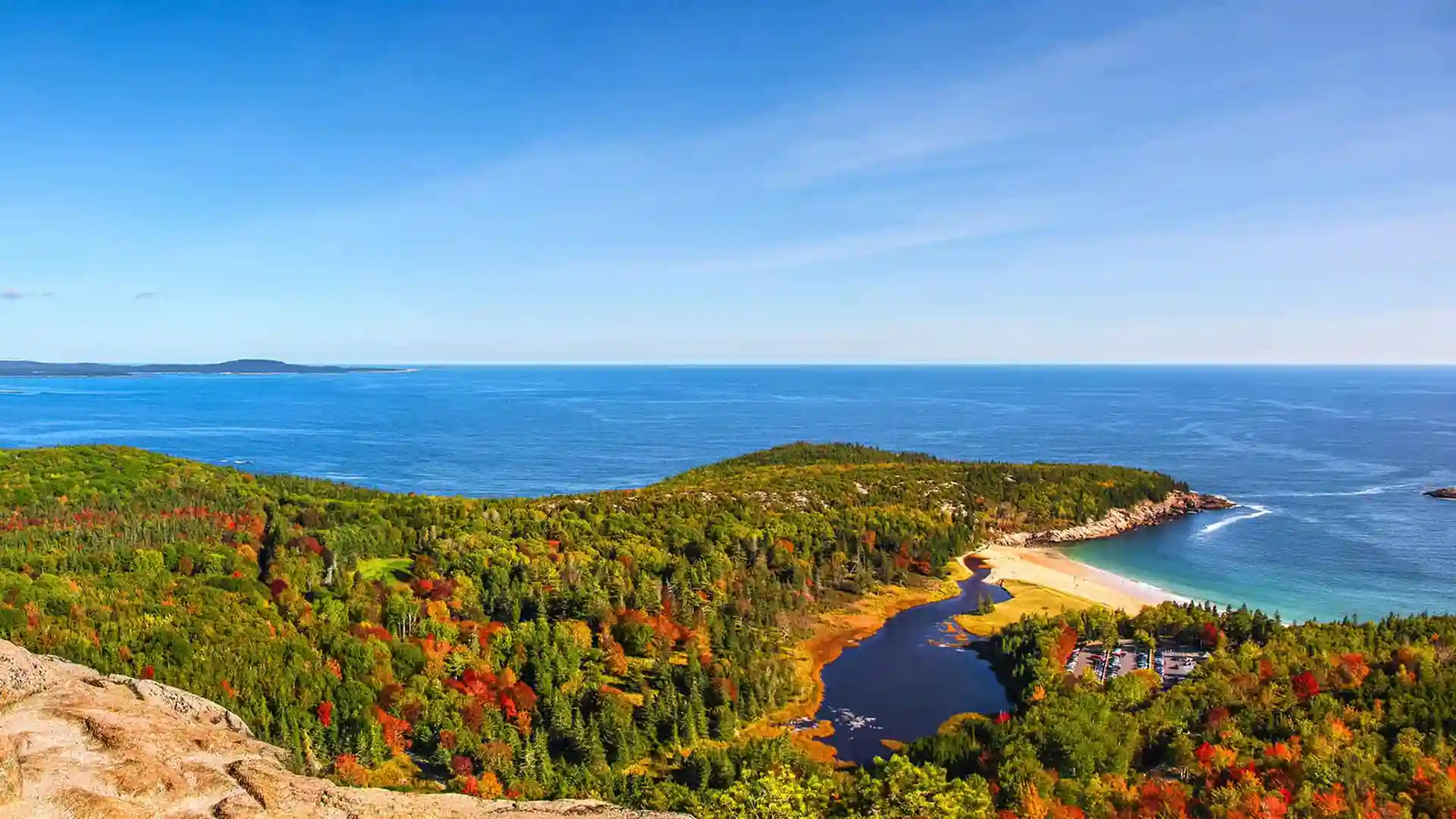 View of northeastern coast in North America, covered by fall foliage, near ocean waters.