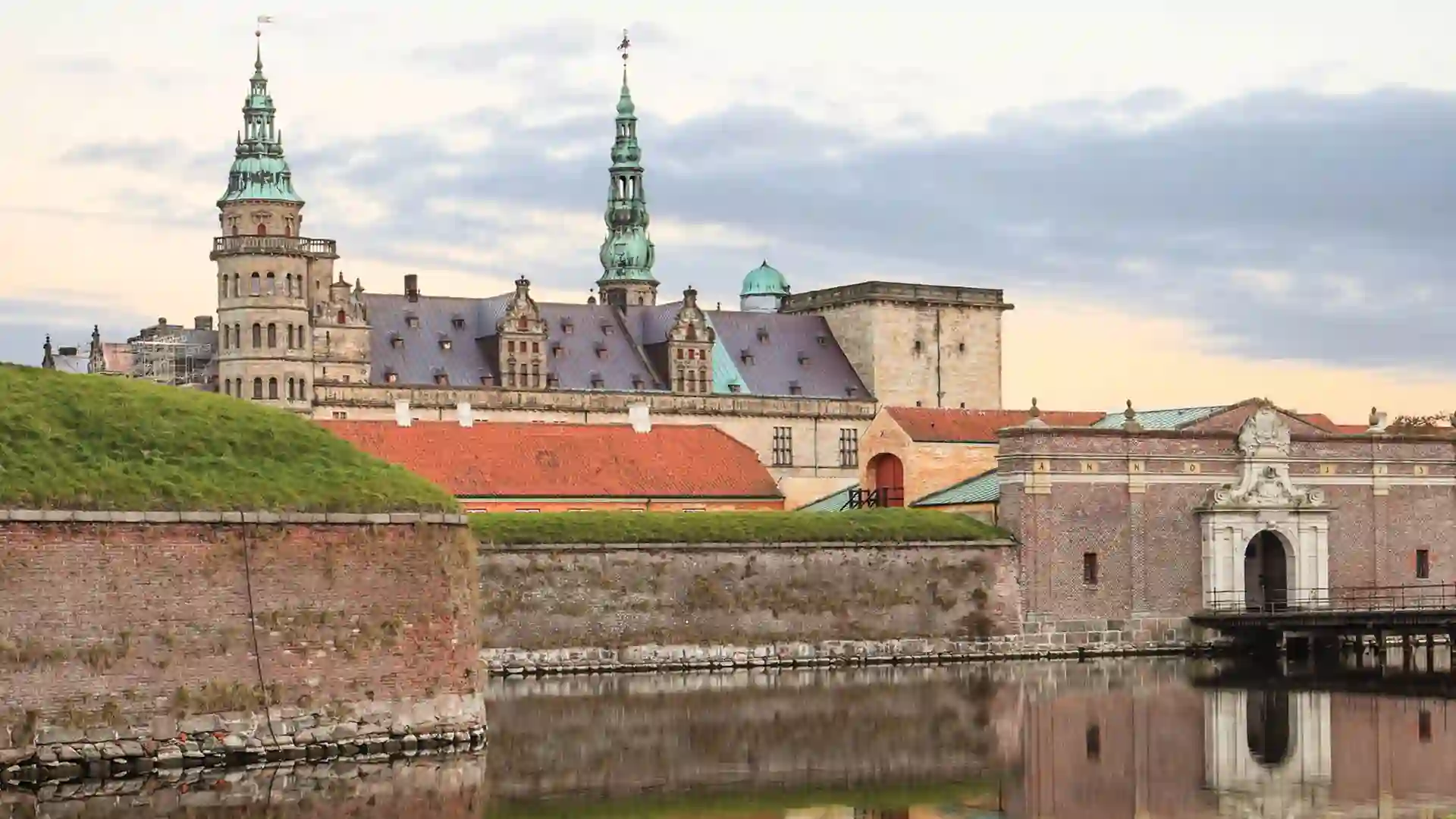 View of castle and green landscape on waterfront with cloudy sky.