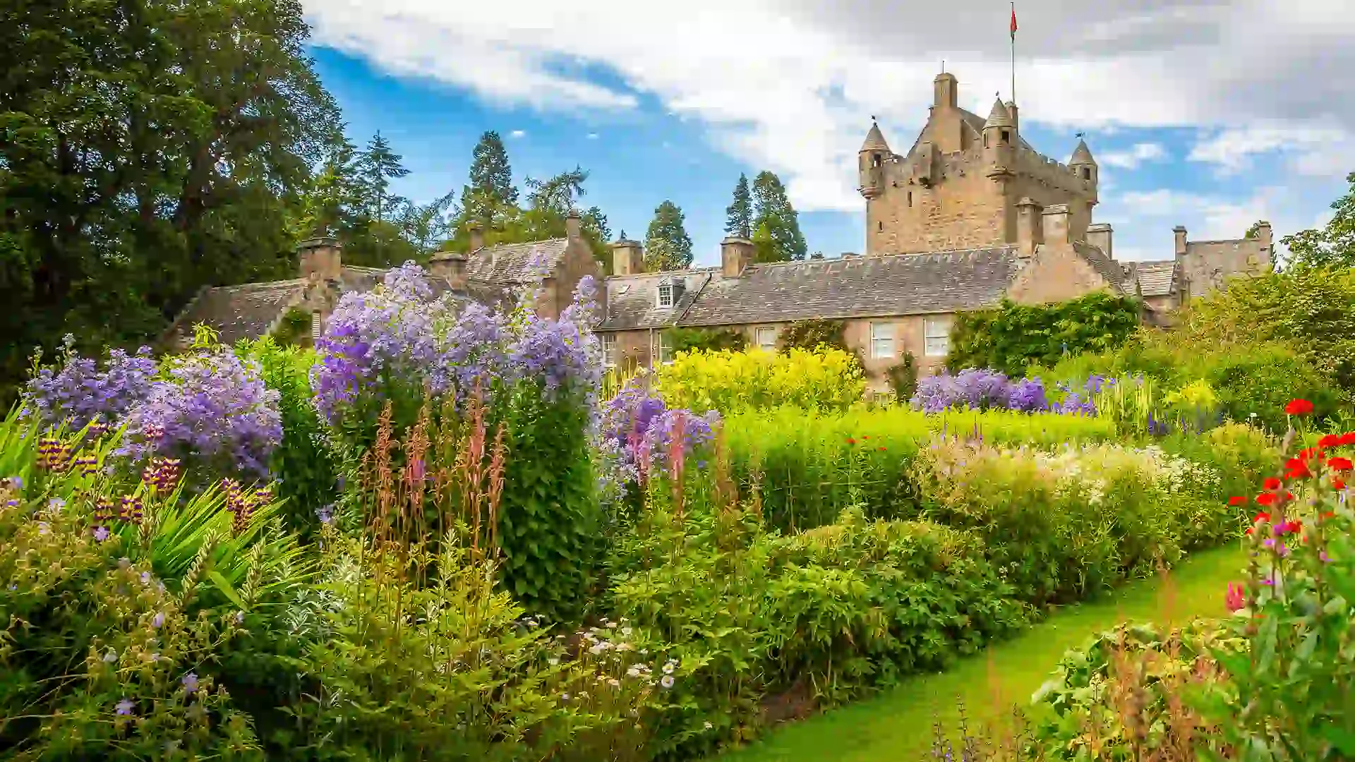 Green garden with purple and orange flowers behind castle.