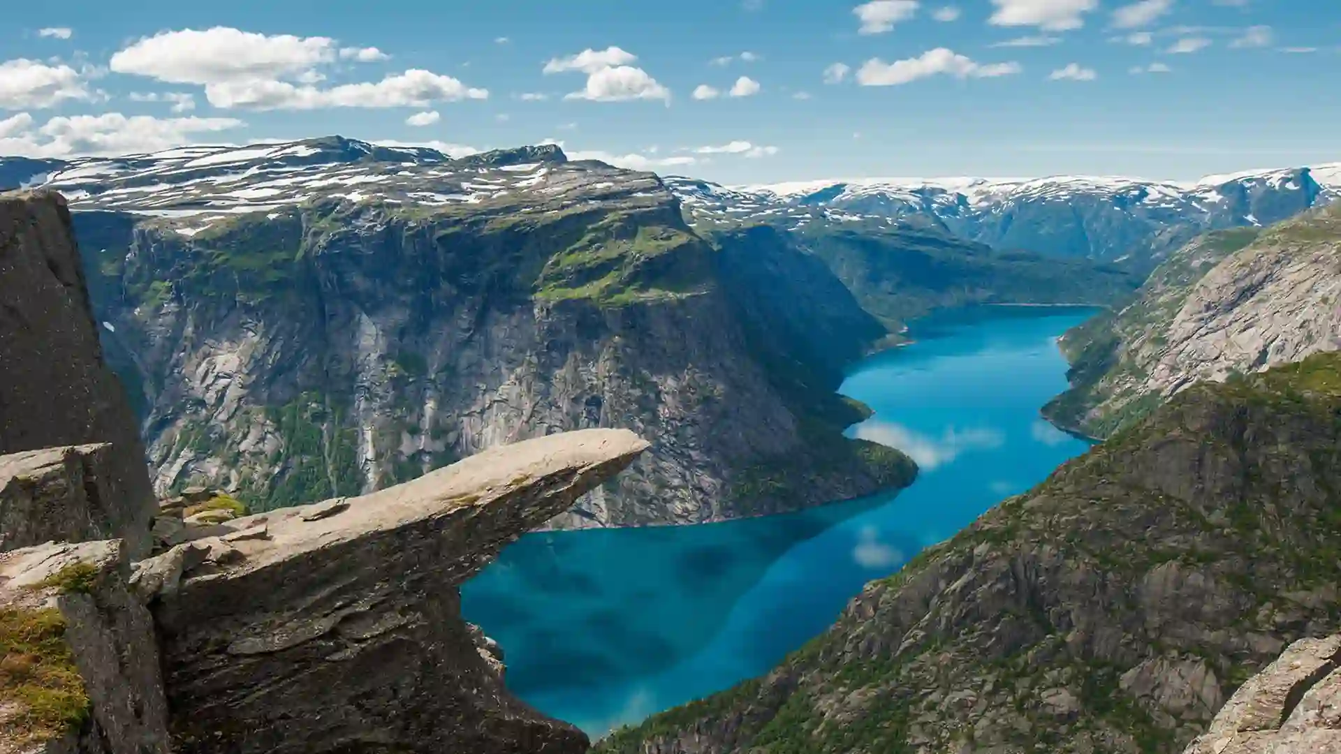 View of peak above mountains with valley of blue water below and blue sky above.