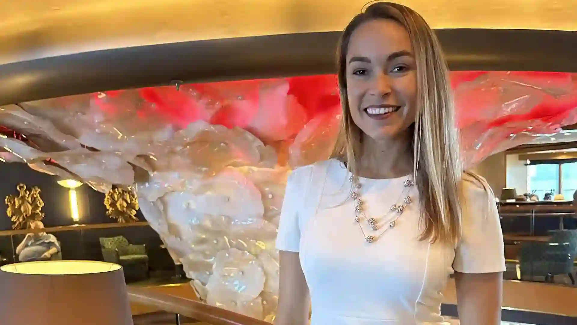 Person in white dress standing in atrium of cruise ship with art in the background.