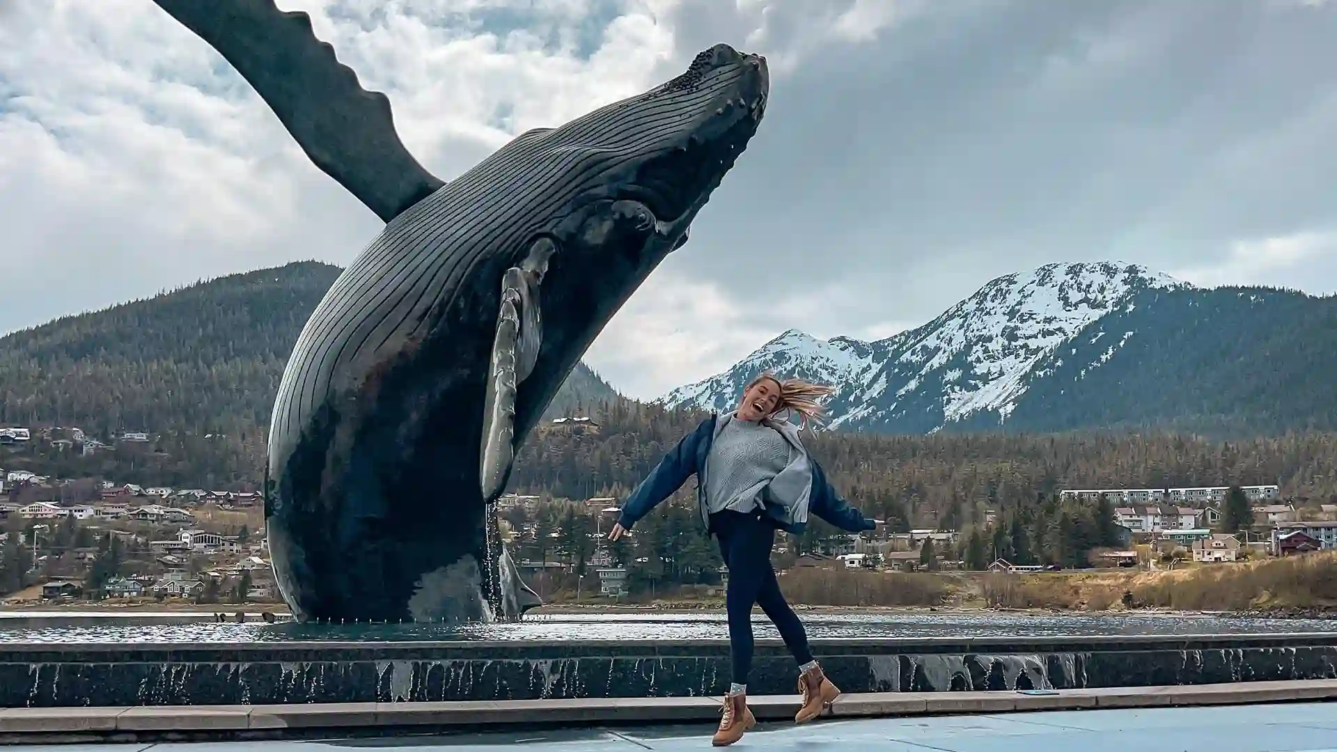 Person jumping in front of whale statue with mountain in background.