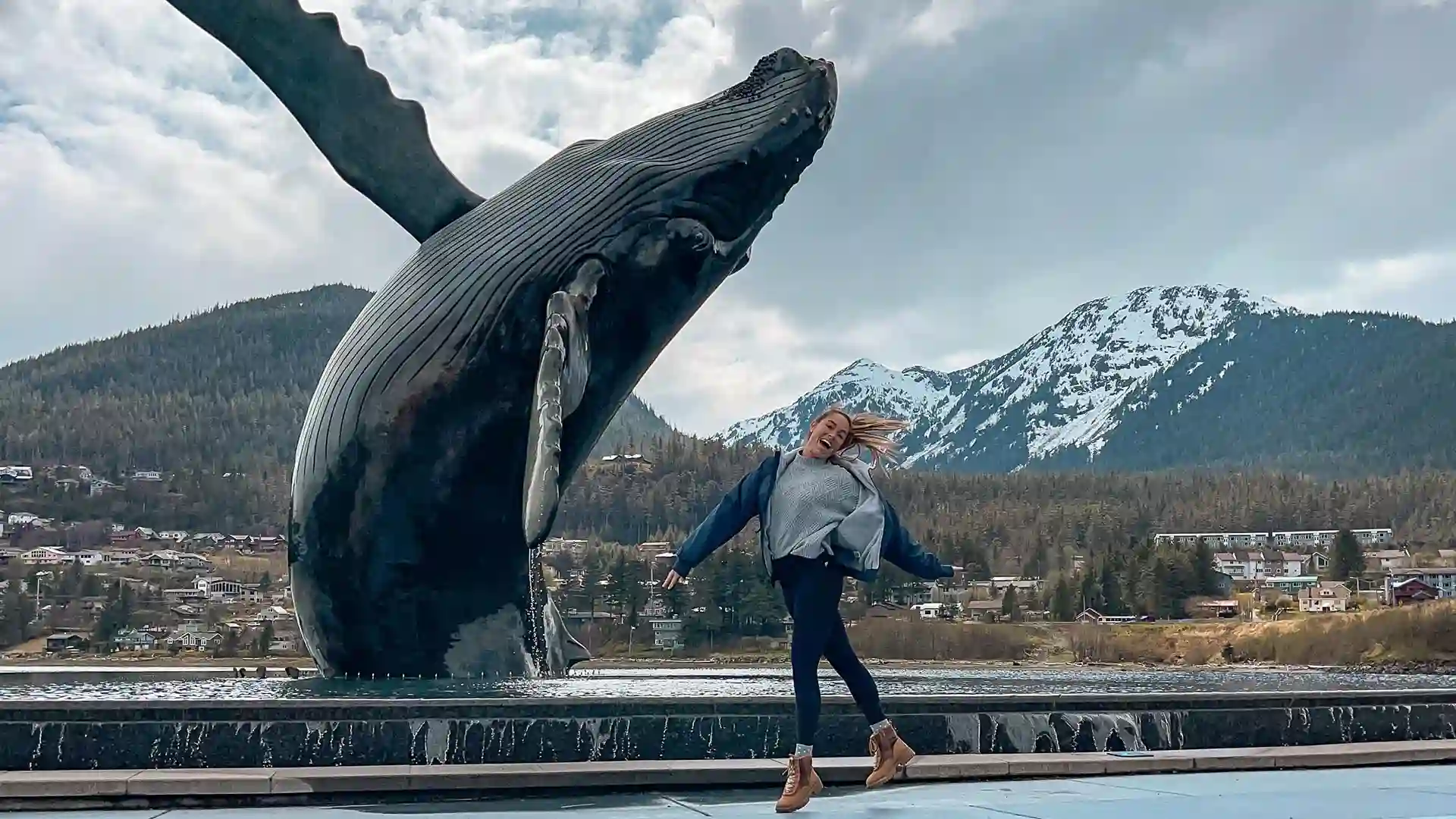 Jordyn, Cruise & Travel Director Person jumping in front of whale statue with mountain in background.