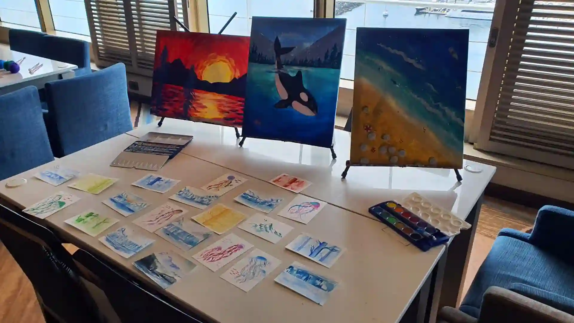 Table covered with art sketches and colorful canvas paintings.