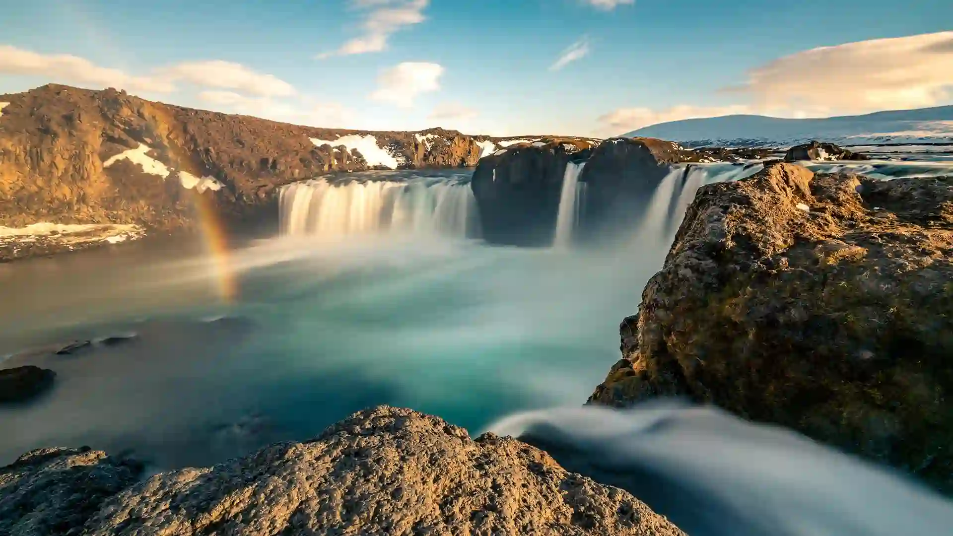 Waterfall in Iceland with rainbow and blue sky.