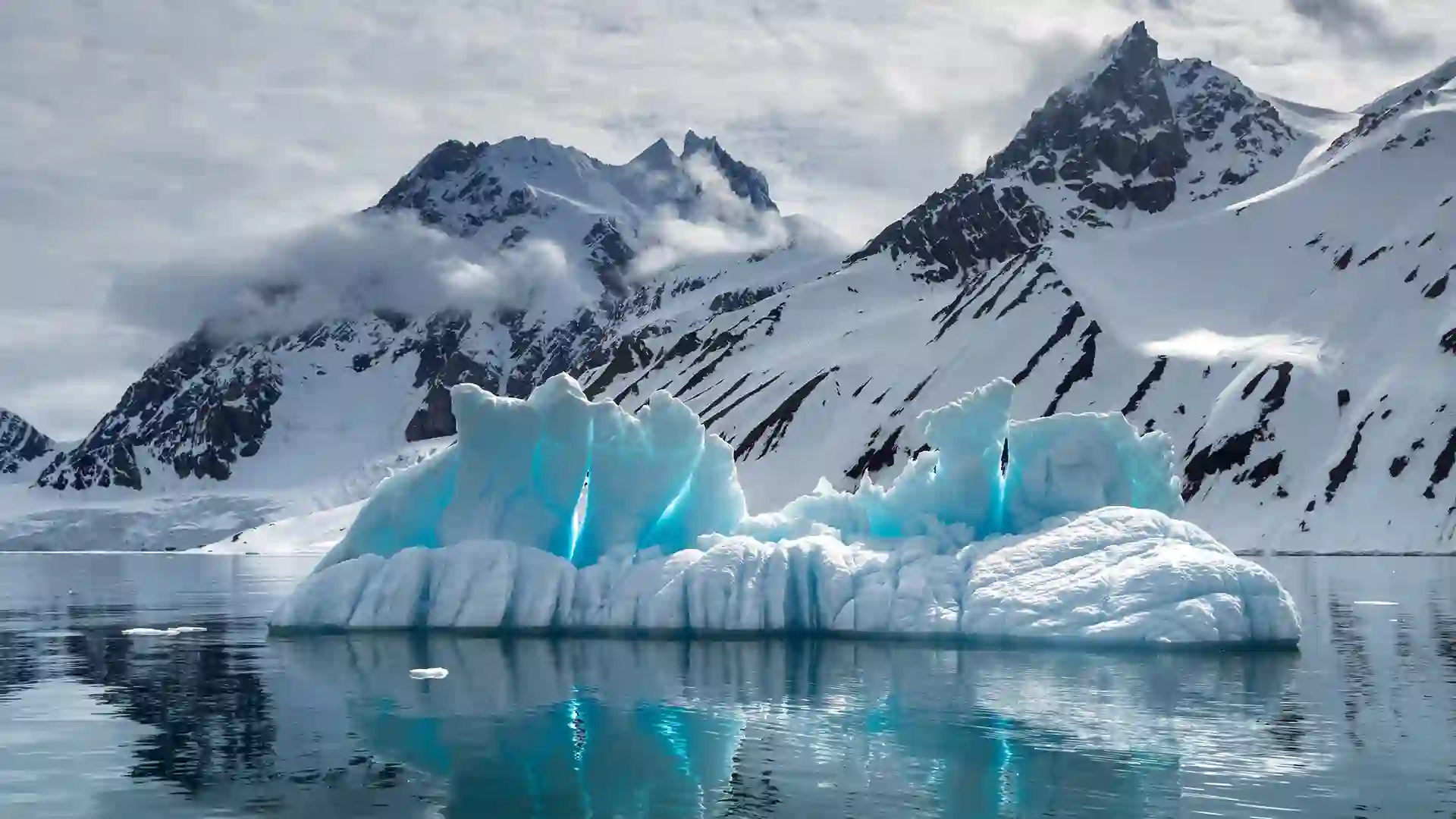Snow-capped mountains and icy-blue glacier with water below.