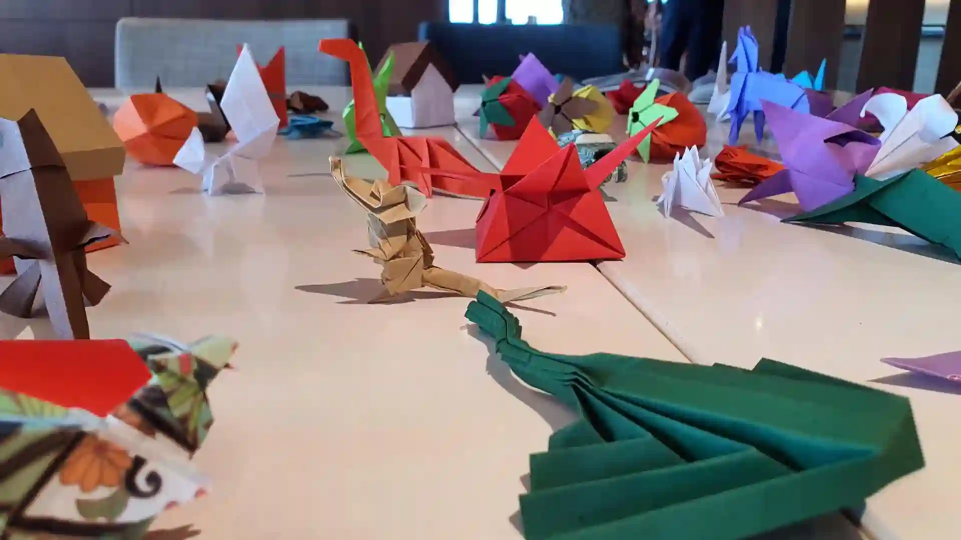Origami Onboard White table covered with colorful paper origami creatures and designs.
