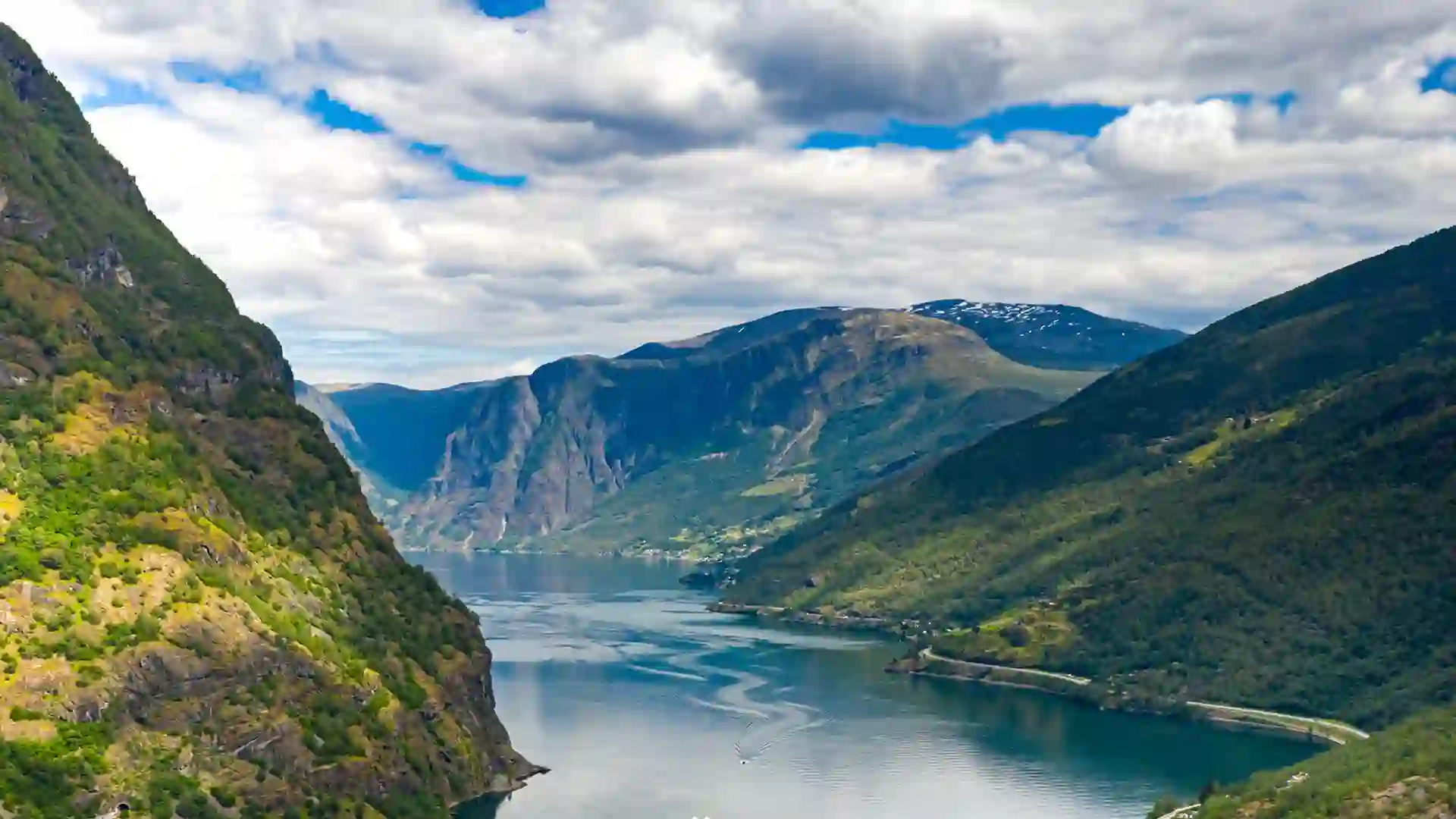 View of green-covered mountains with valley of water below under cloudy sky.