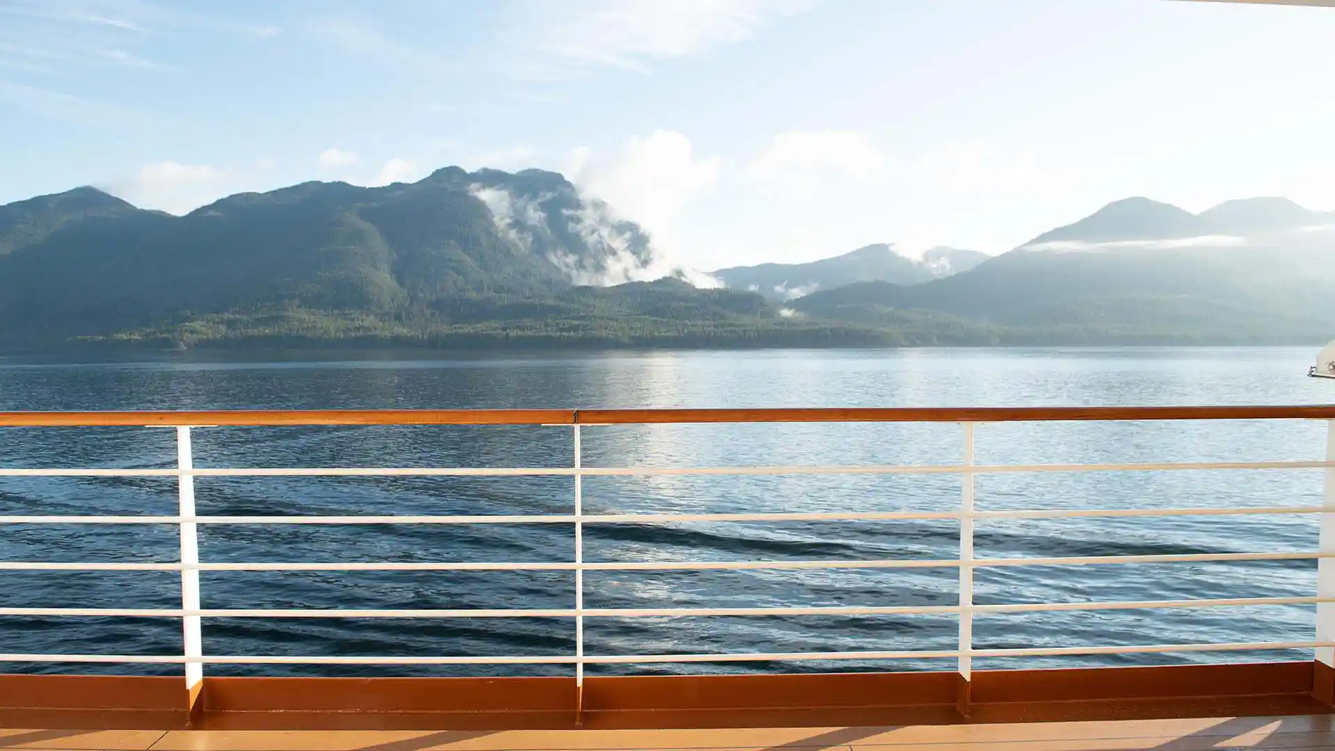 View from deck of ship overlooking water with green landscape in the background.