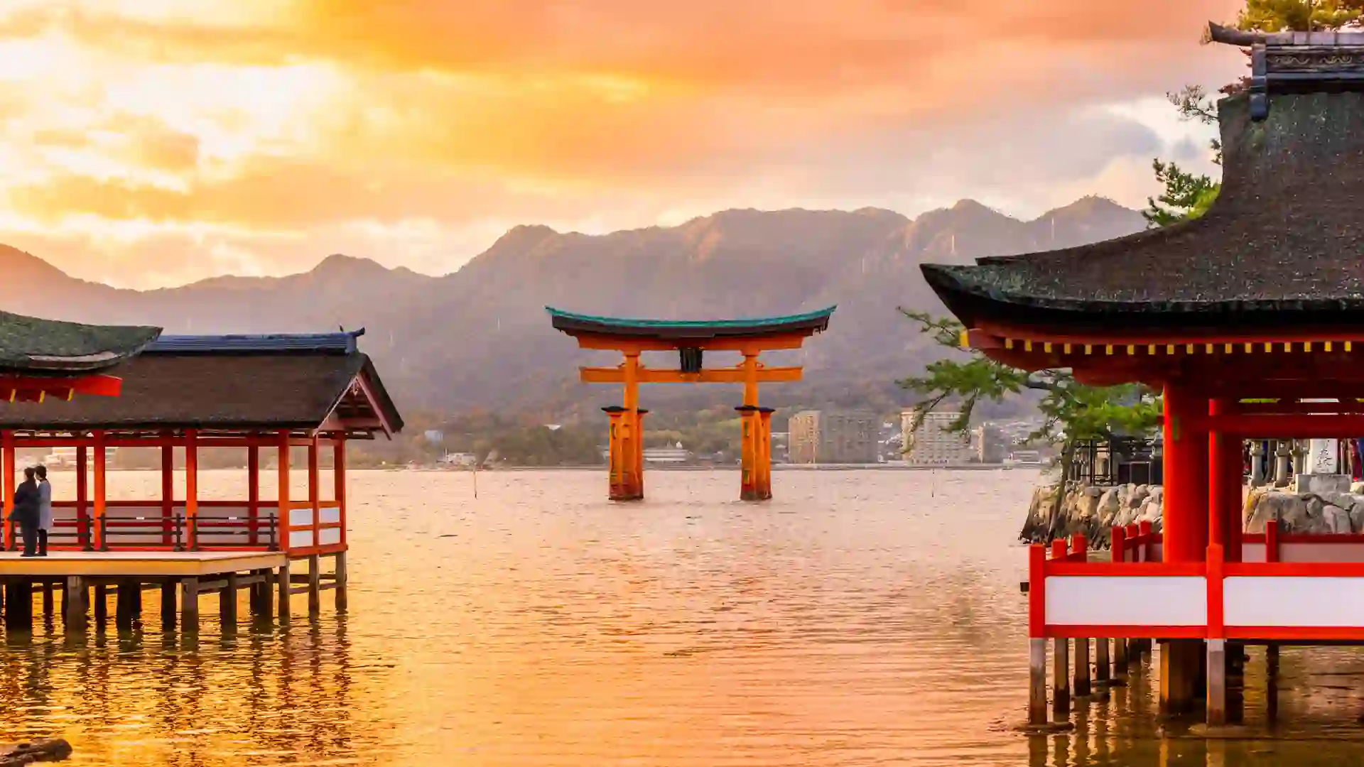 Torii Gate in Japan Gate landmark in water with mountains and sunset in background.