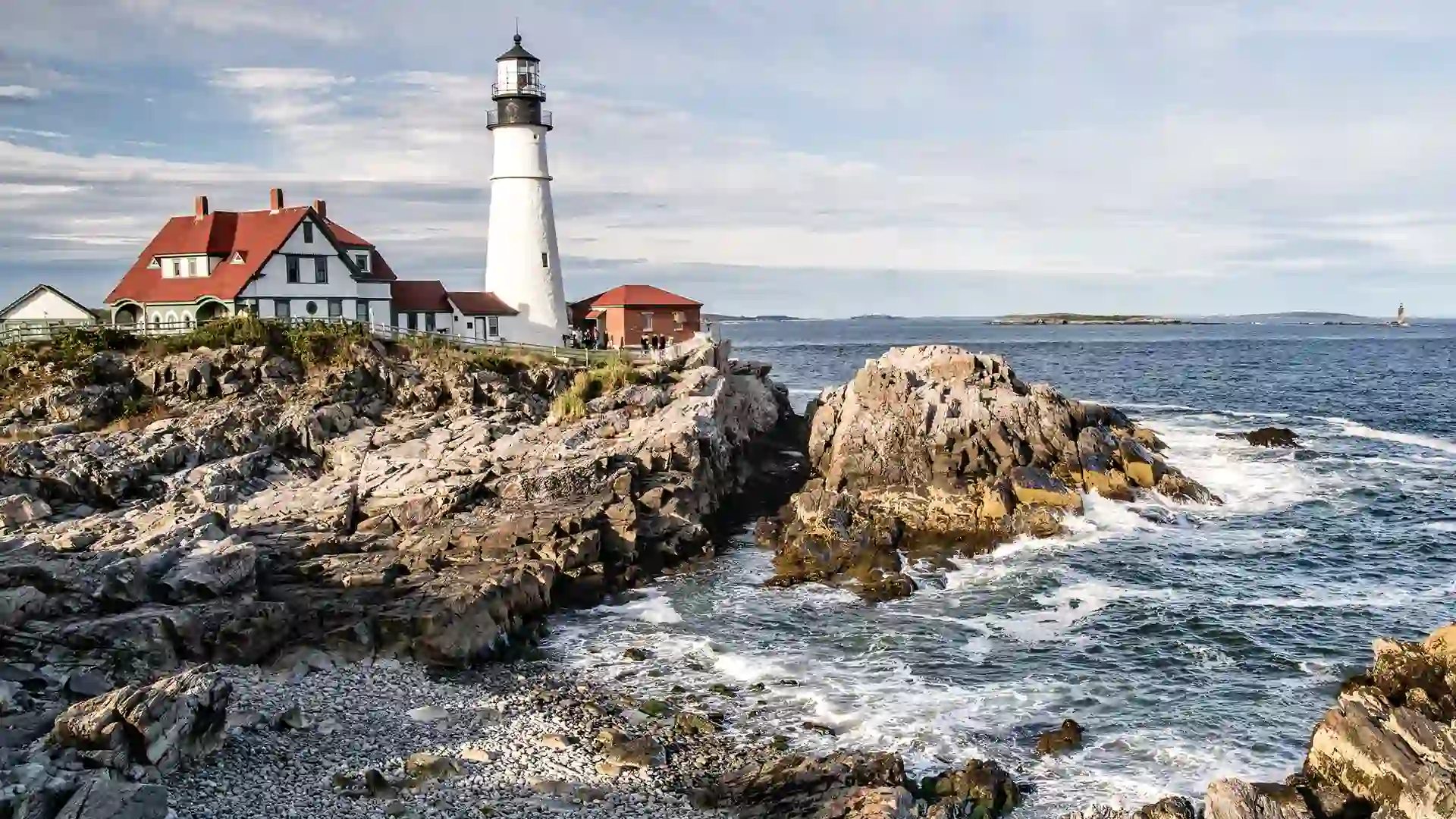 View of a tall white and black lighthouse overlooking a rocky shore.