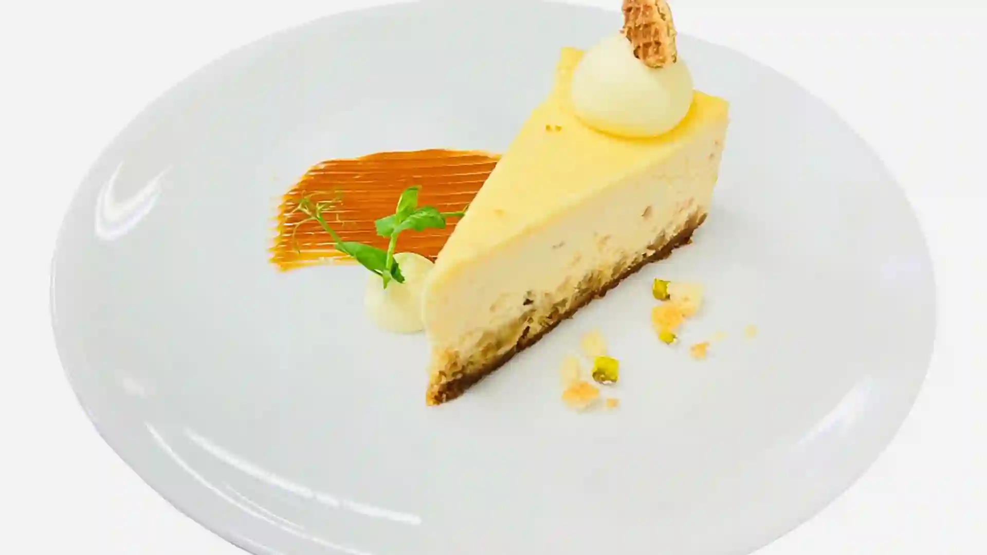 Stroopwafel Cheesecake Yellow cheesecake with caramel sauce on white plate.