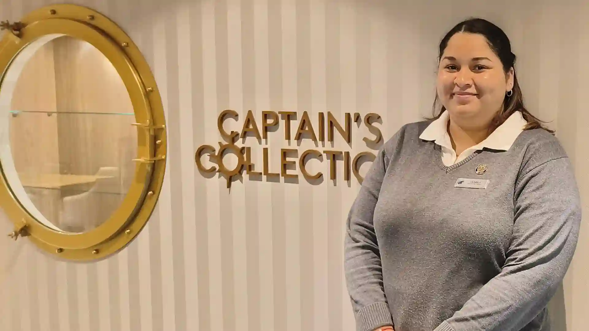 Person in gray and white uniform standing in front of wall with gold-colored artwork.