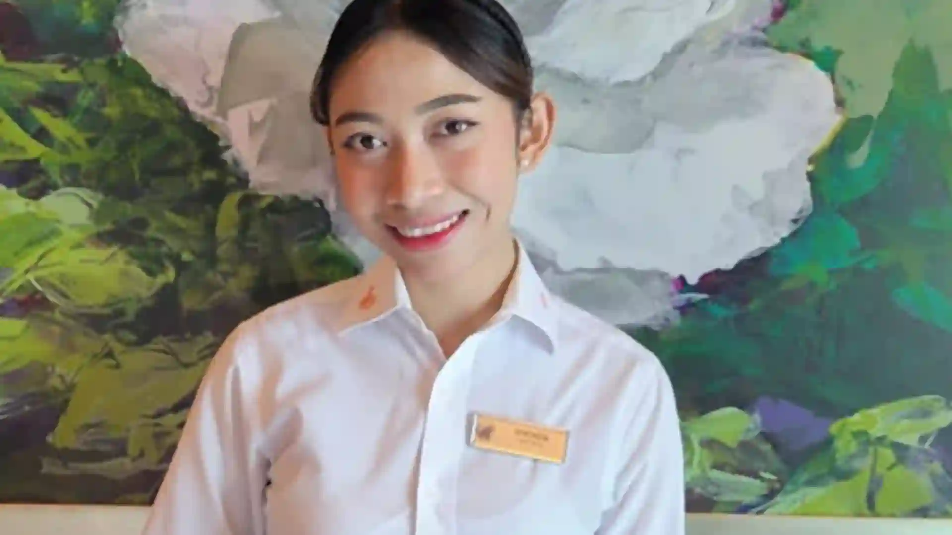 Person in white collared top in front of white floral artwork.