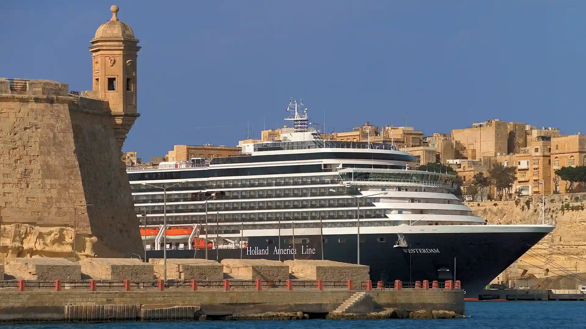Holland America Line Cruise Ship in Malta View of cruise ship sailing on blue water near island port.