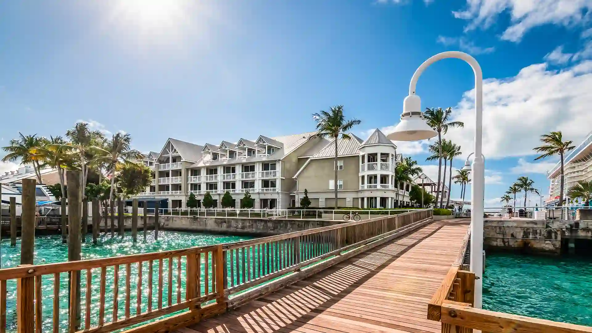 Key West View from wooden dock overlooking blue waters, white building and palm trees.