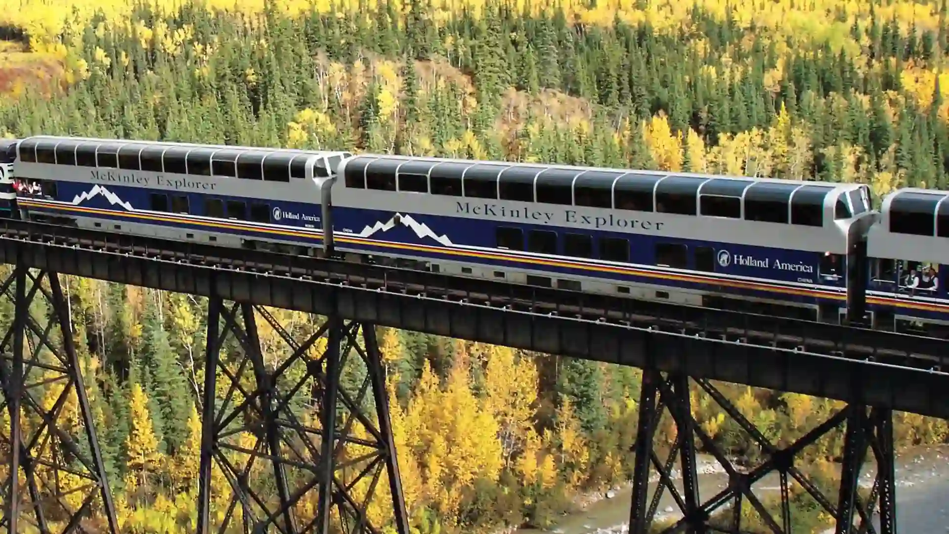 View of train crossing bridge with green-covered landscape in the background and river below it.