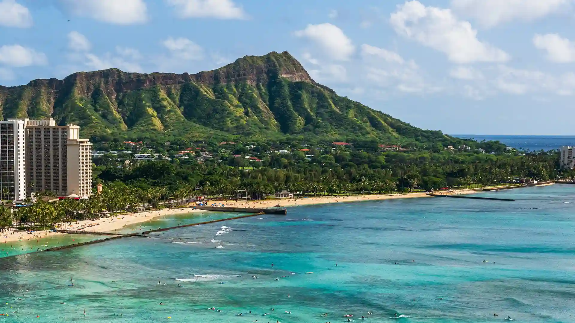 View of light blue ocean waters along the shore in Honolulu with a lush green landscape in the background.