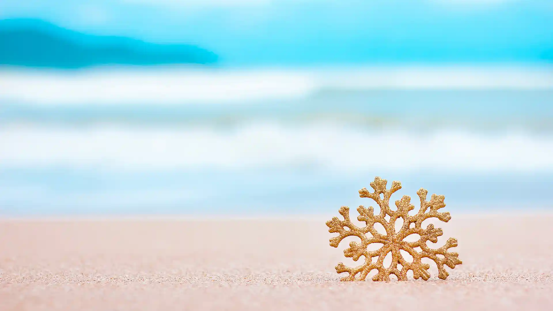 Golden snowflake in the sand with ocean waves in the background.