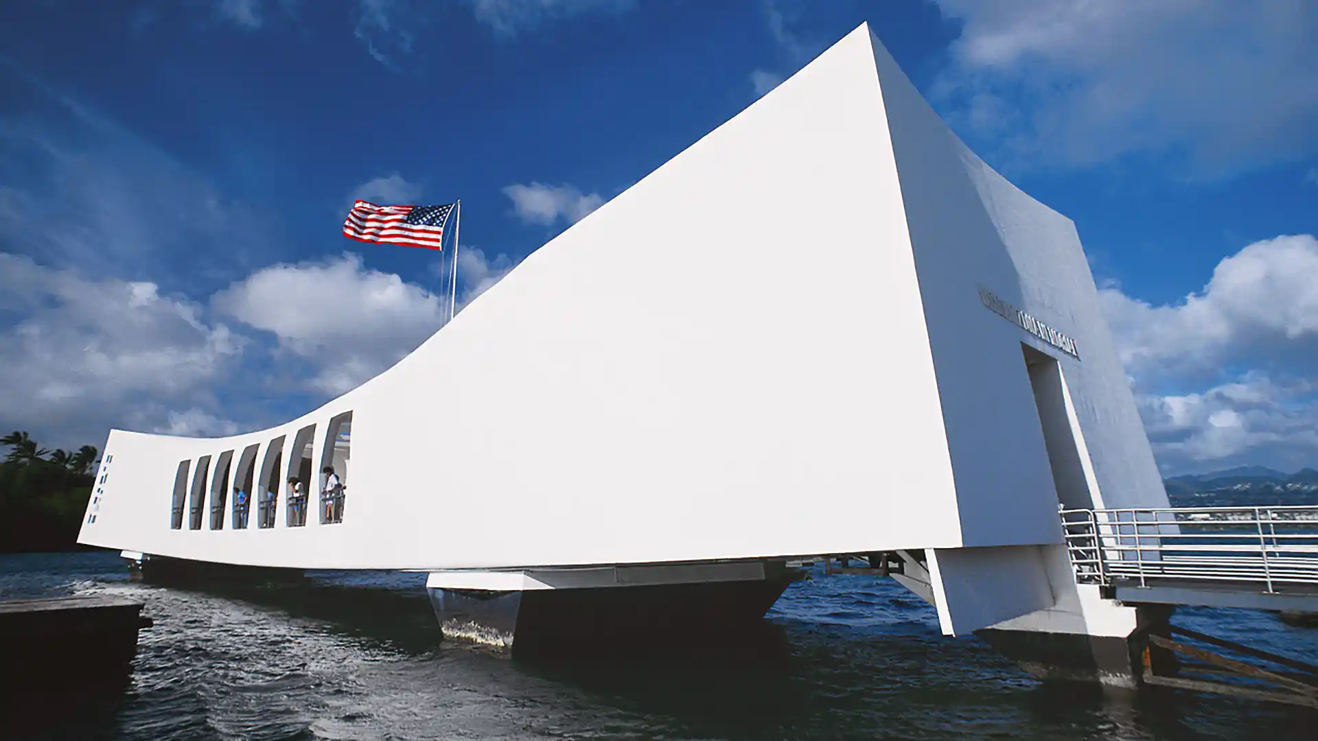 View of white structure with waving American flag above at Pearl Harbor Memorial in Hawaii.
