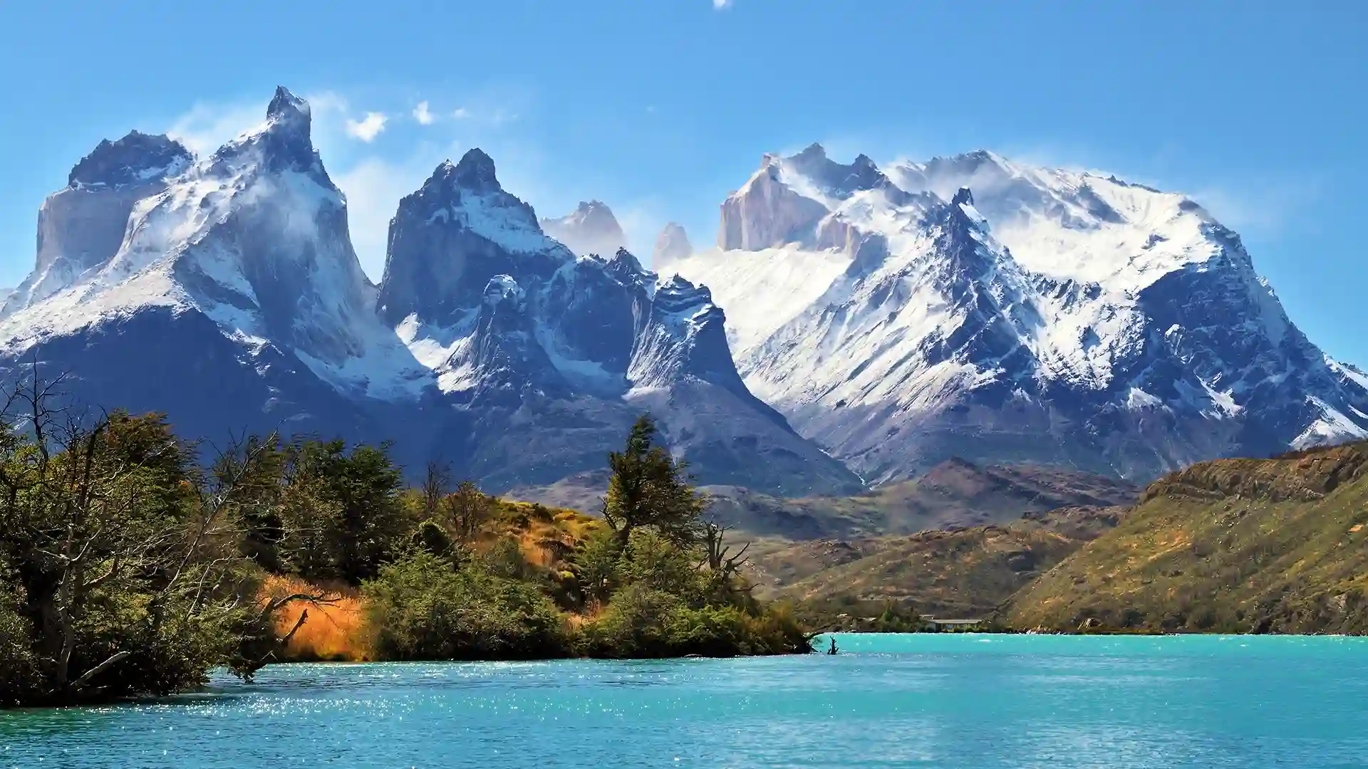 View of snowcapped mountains with green vegetation and water in the valley at Torres del Paine National Park in South America.