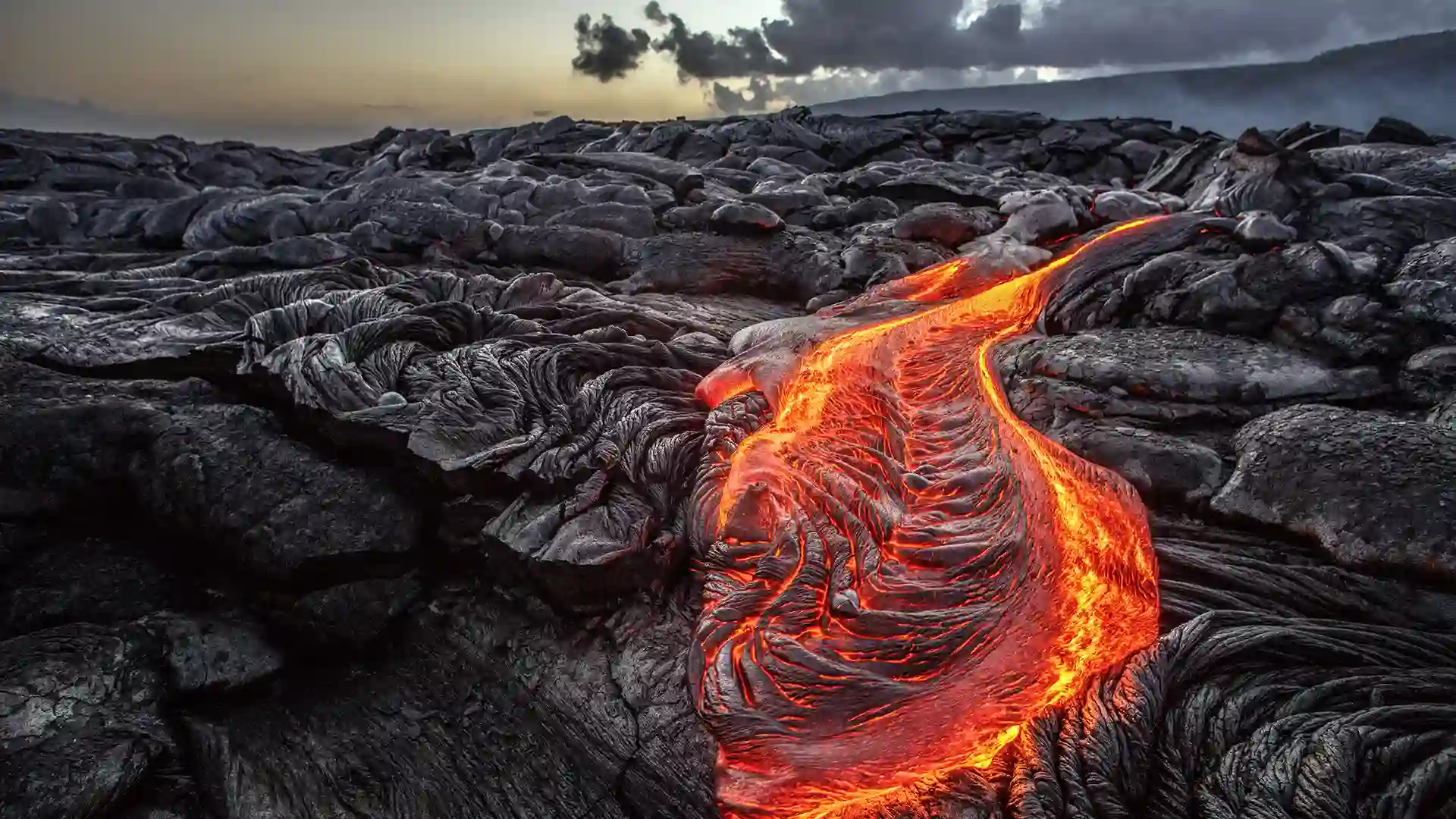 View of orange lava flowing across black volcanic rock in Hawaii.