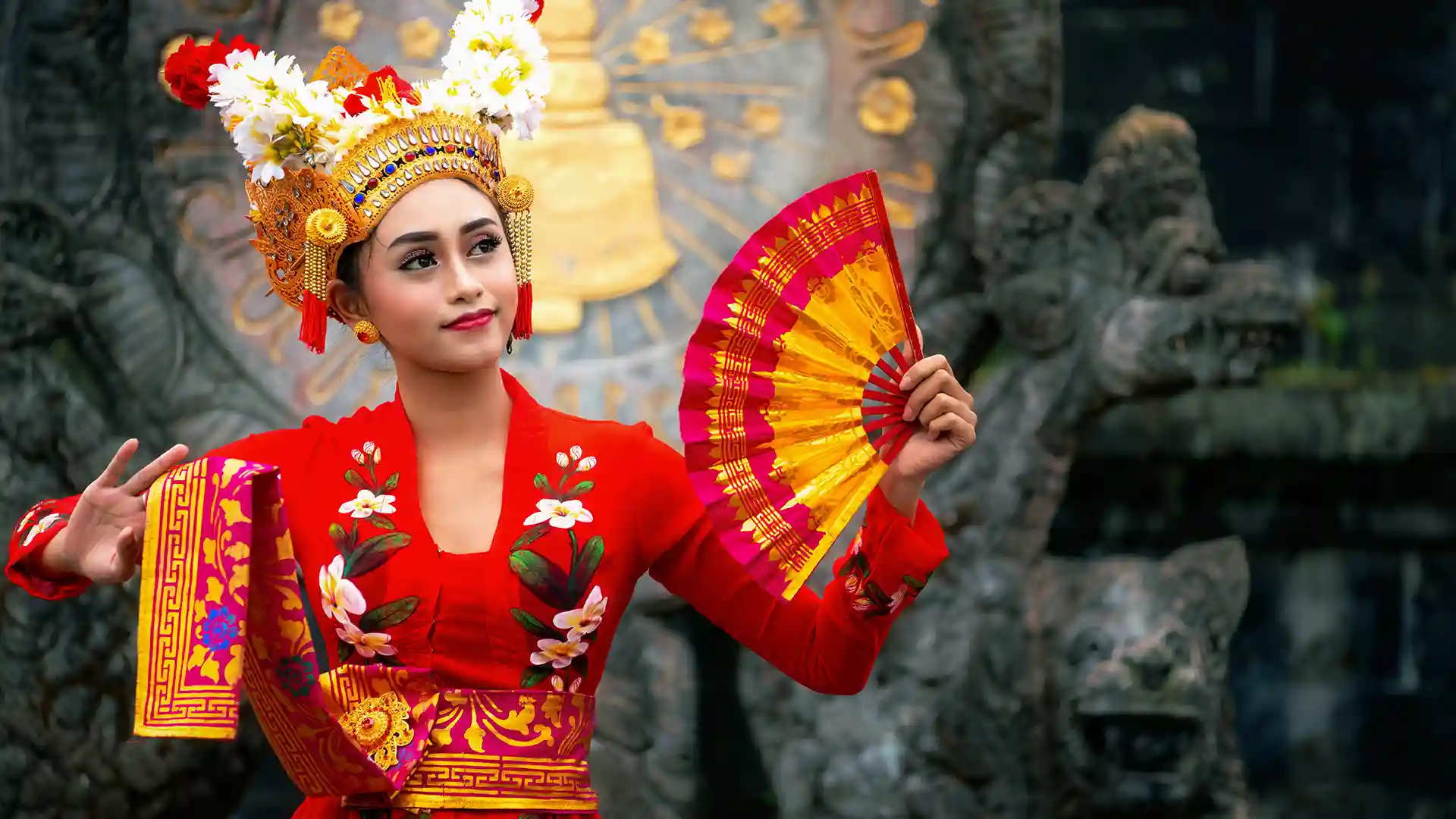 Person in embroidered red dress holding a red and yellow folding fan representing unique culture in Asia.