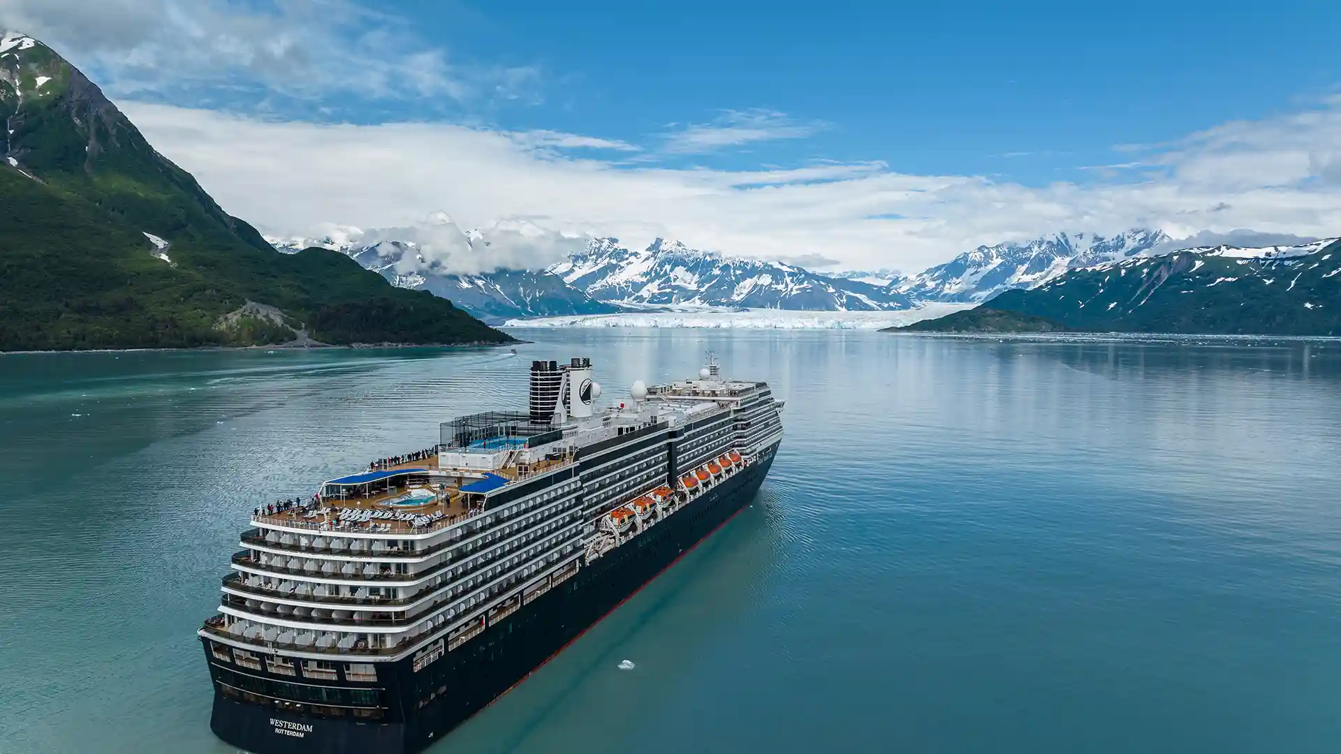 View of Holland America Line cruise ship in Alaska surrounded by snowcapped mountains.