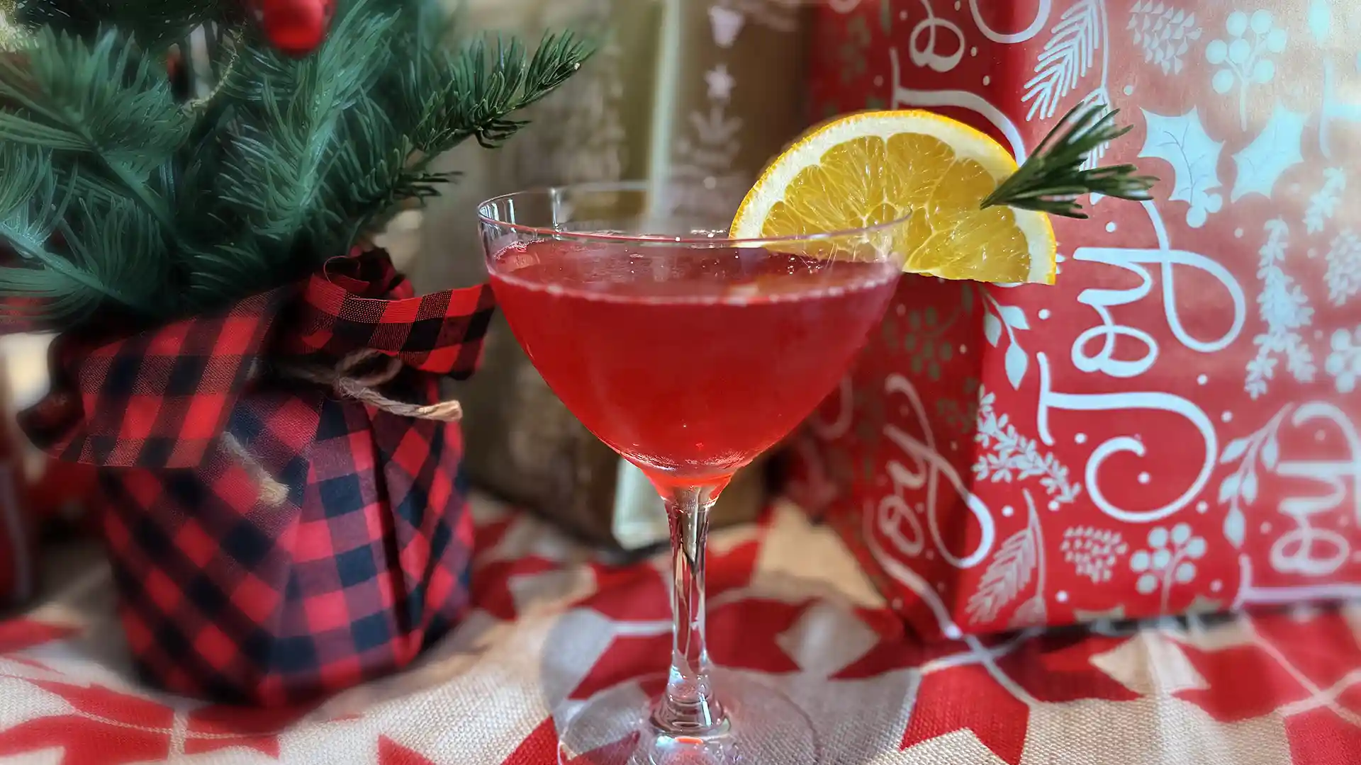 Mistletoe Martini Holiday Cocktail Orange-colored cocktail in martini glass with rosemary sprig, orange slice and cranberries.