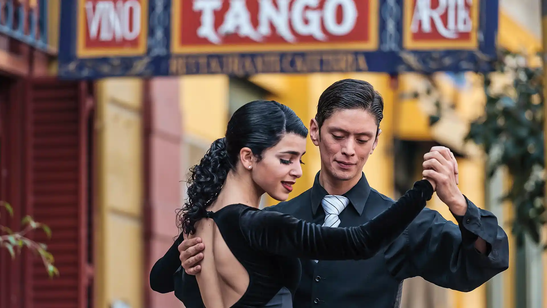 Holiday Gift Ideas Dance Lessons Two people dressed in black dancing in front of tango sign.
