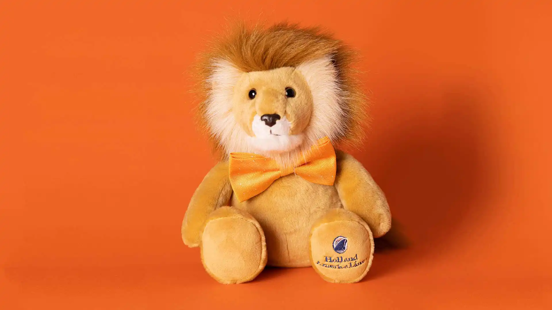 Lewie the Lion stuffed animal, Holland America Line's mascot, with orange bowtie and background.