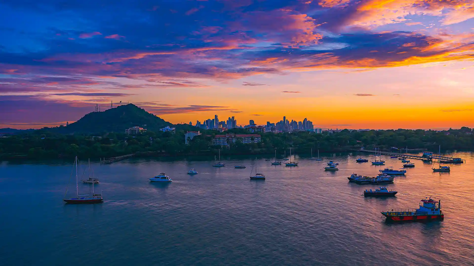 View of a sunrise over Panama where boats float on glistening water reflecting orange hues.
