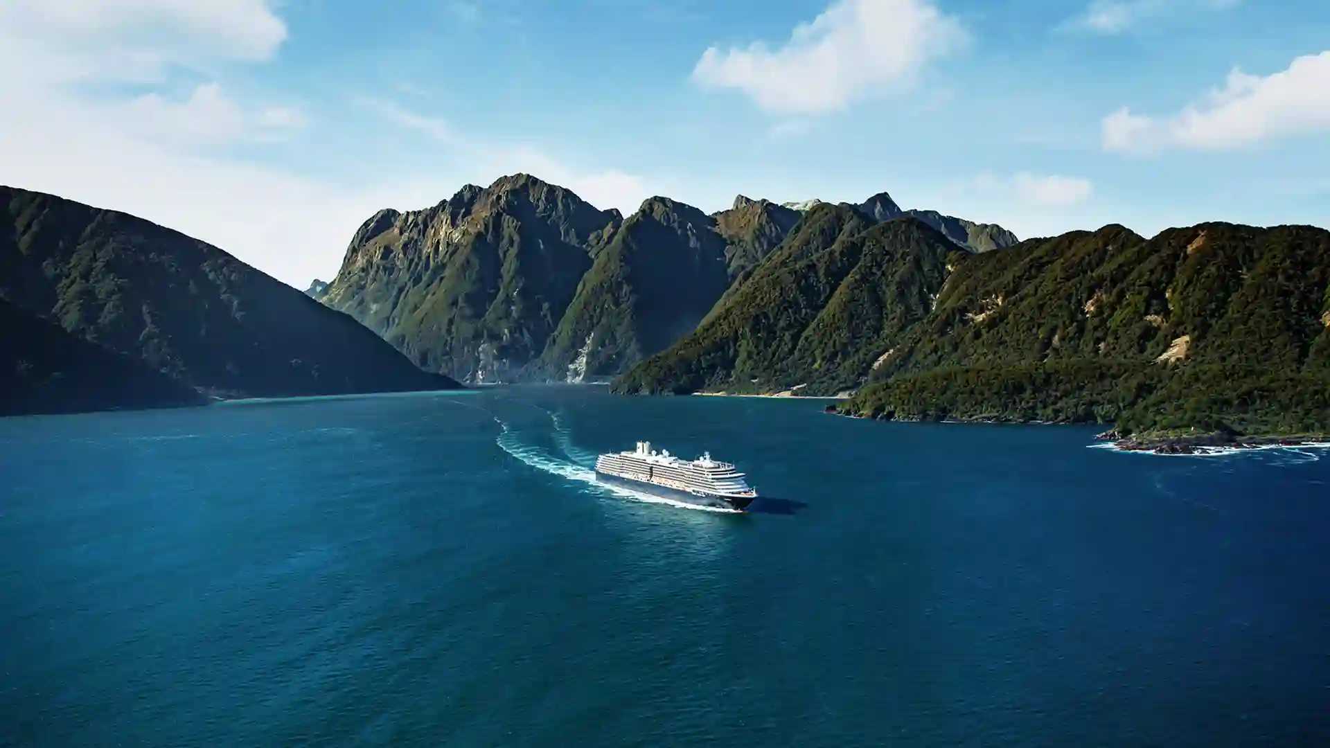 View of Holland America Line cruise ship sailing around New Zealand's lush landscape.
