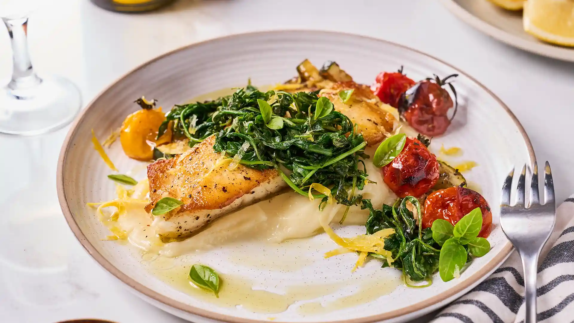 View of Holland America Line's Gold Gala Pan-Seared Sea Bass meal with cherry tomatoes and arugula on white plate.