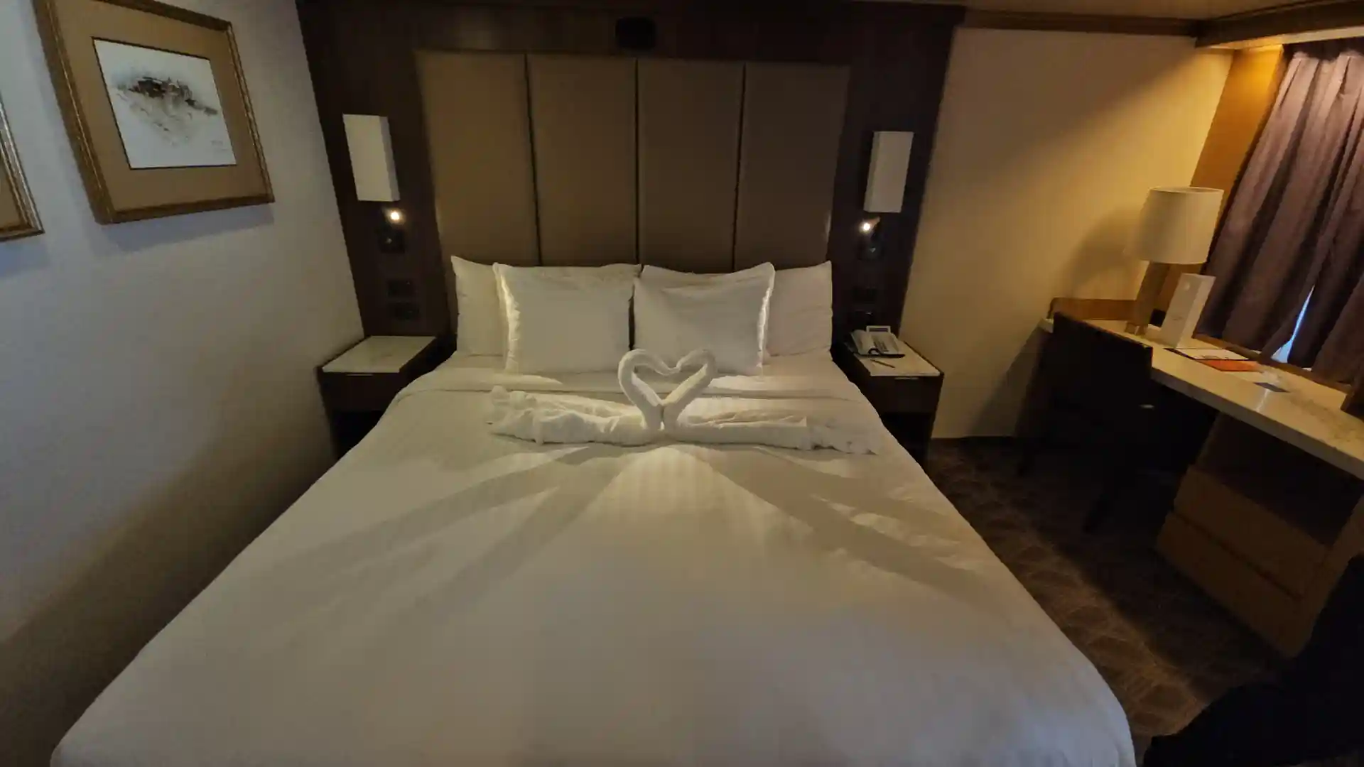 View of towels in the shape of kissing swans on a bed in a Holland America Line stateroom.