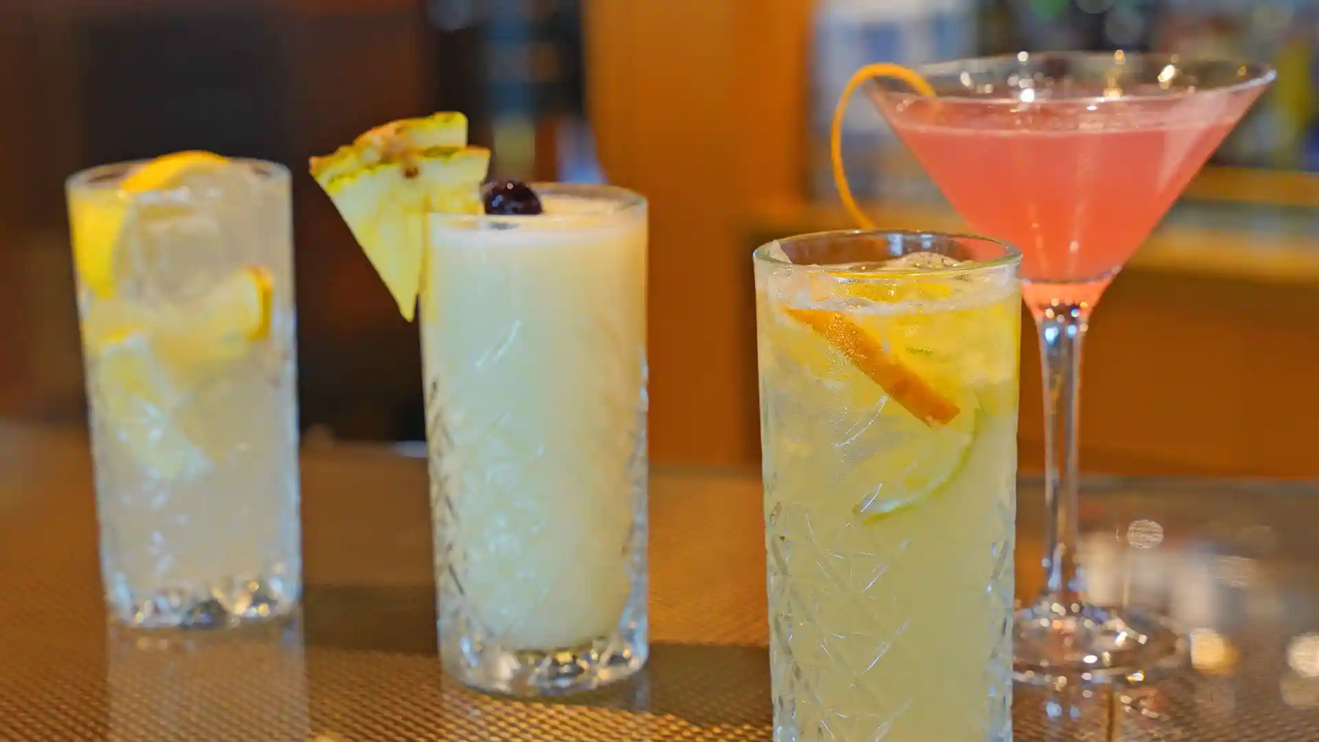 Different mocktails in drinking glasses on bar with garnish.