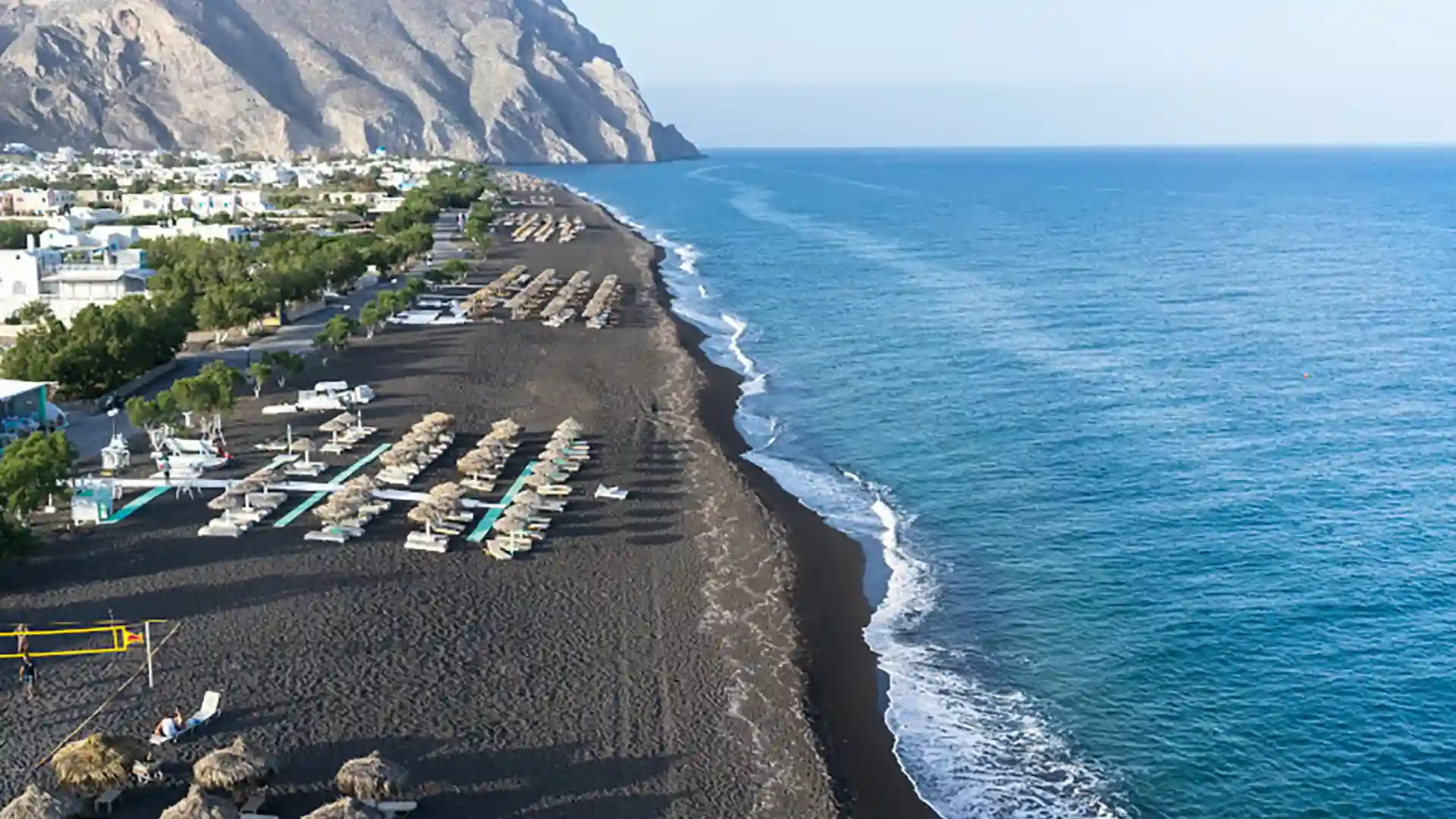 View of Perissa Beach in the Mediterranean, where black sand meets bright blue ocean water.